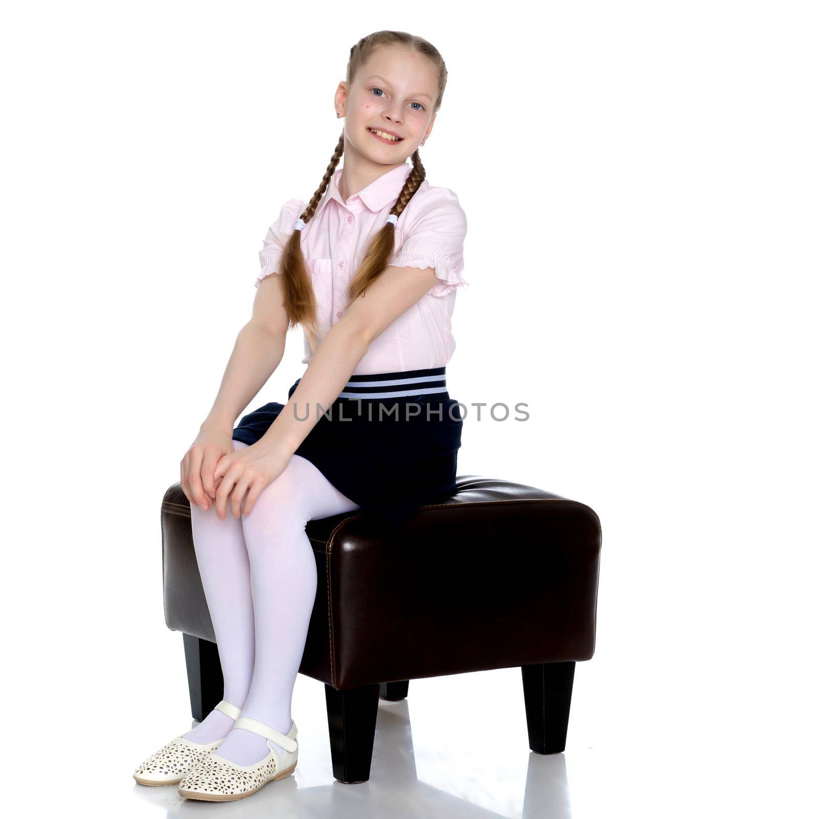 Beautiful schoolgirl girl with long pigtails sitting on the couch. The concept of school fashion, children's emotions. Isolated on white background.