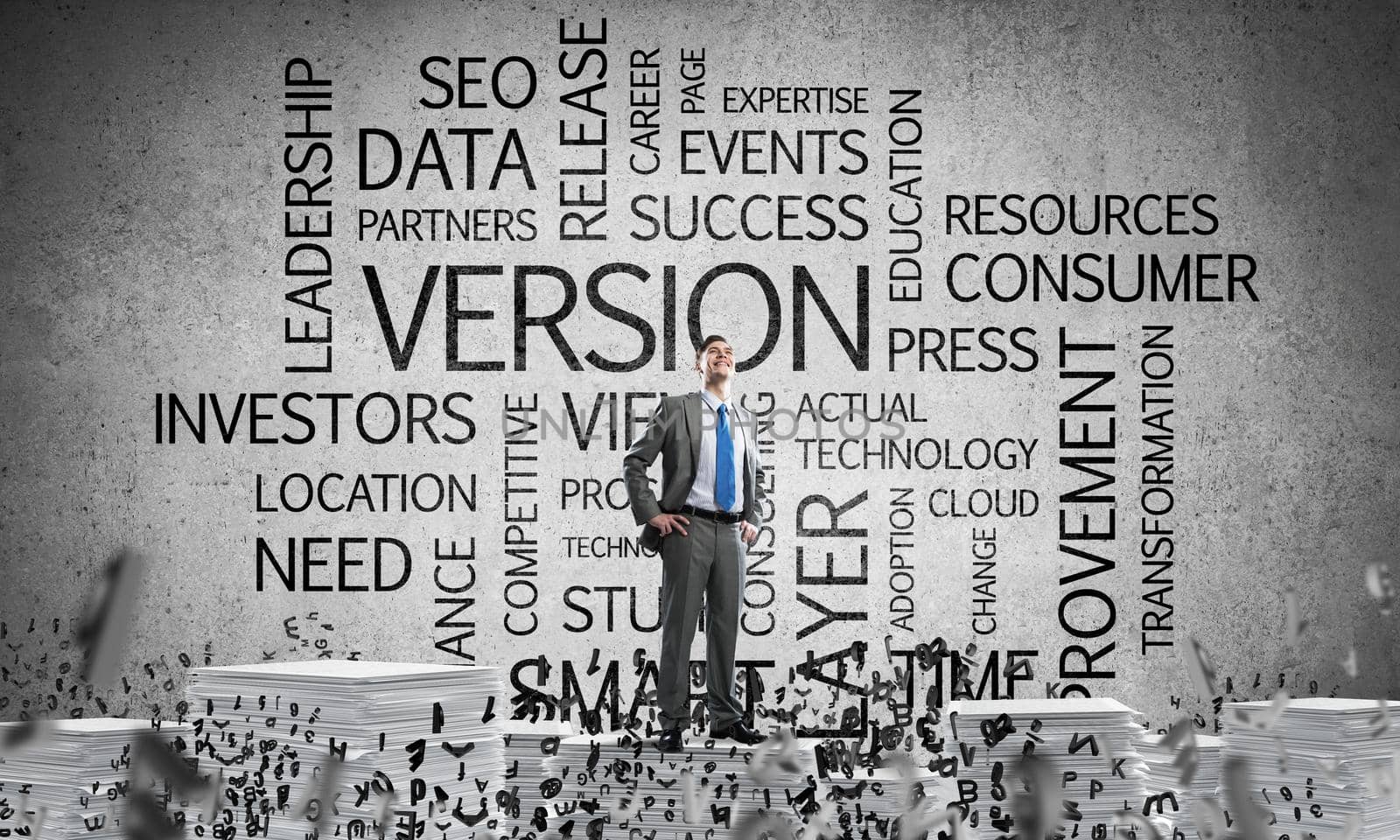 Confident businessman in suit standing on pile of documents among flying letters with business related terms on background. Mixed media.
