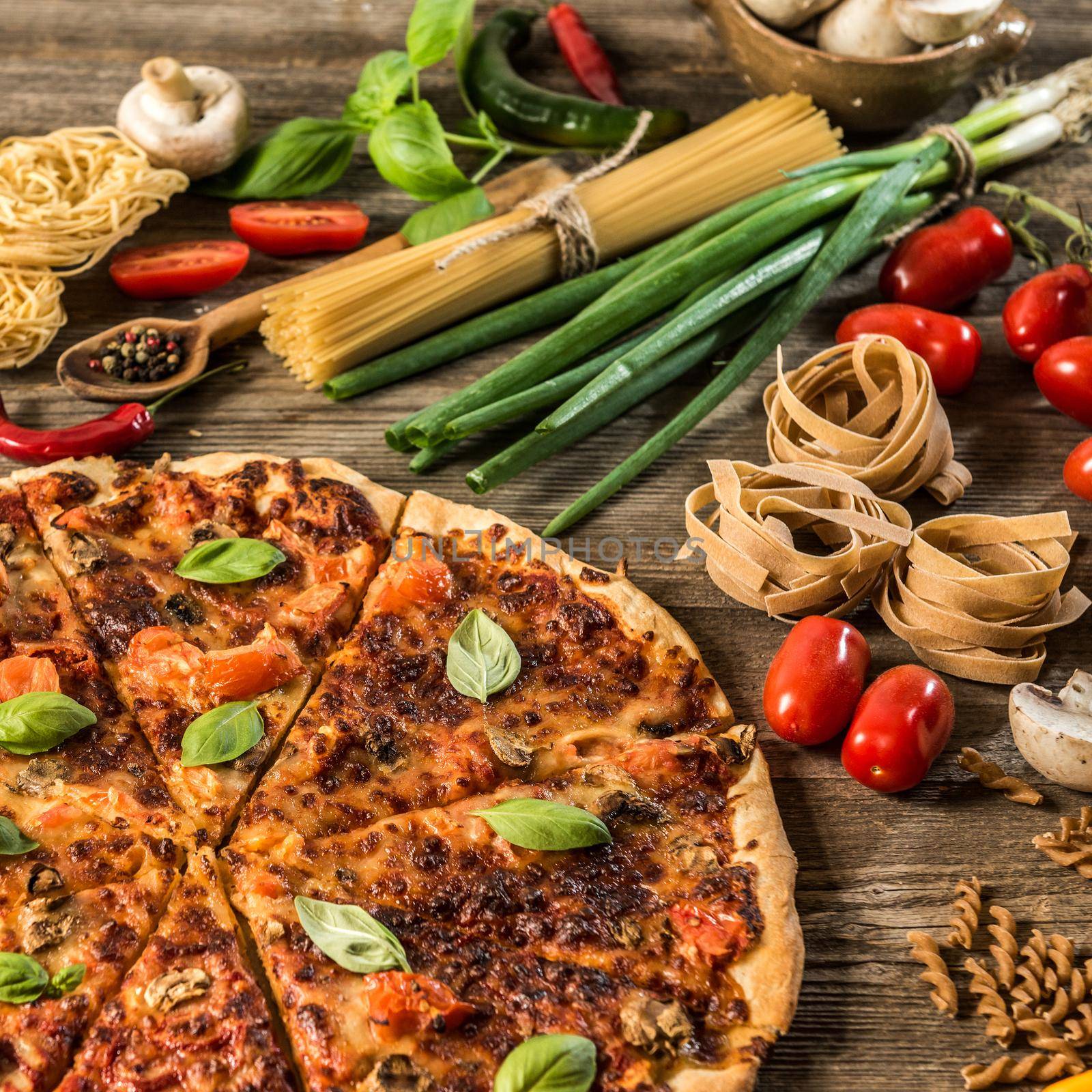 Italian food background with pizza, raw pasta and vegetables on wooden table