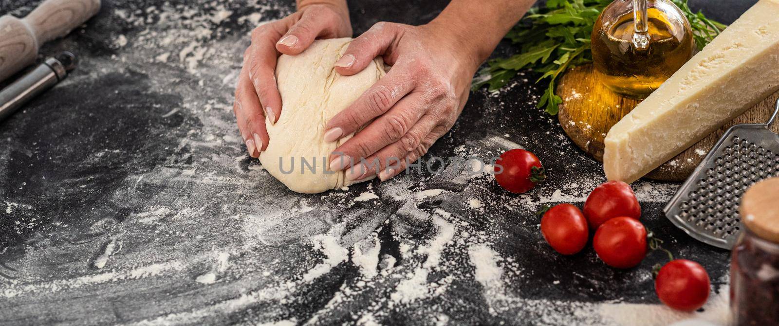 Top view of woman kneading dough for pizza baking on black floured background