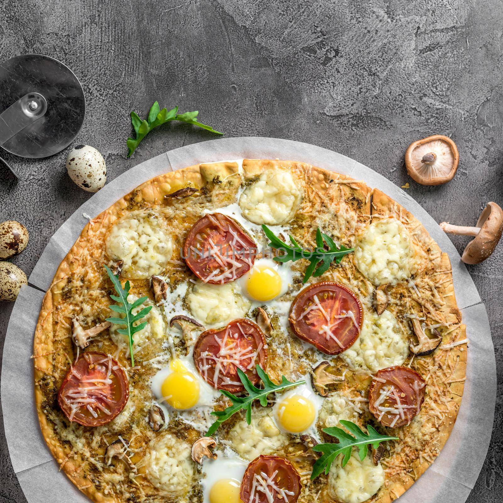 Homemade pizza with mushrooms and mozzarella decorated with arugula on a concrete background with food ingredients