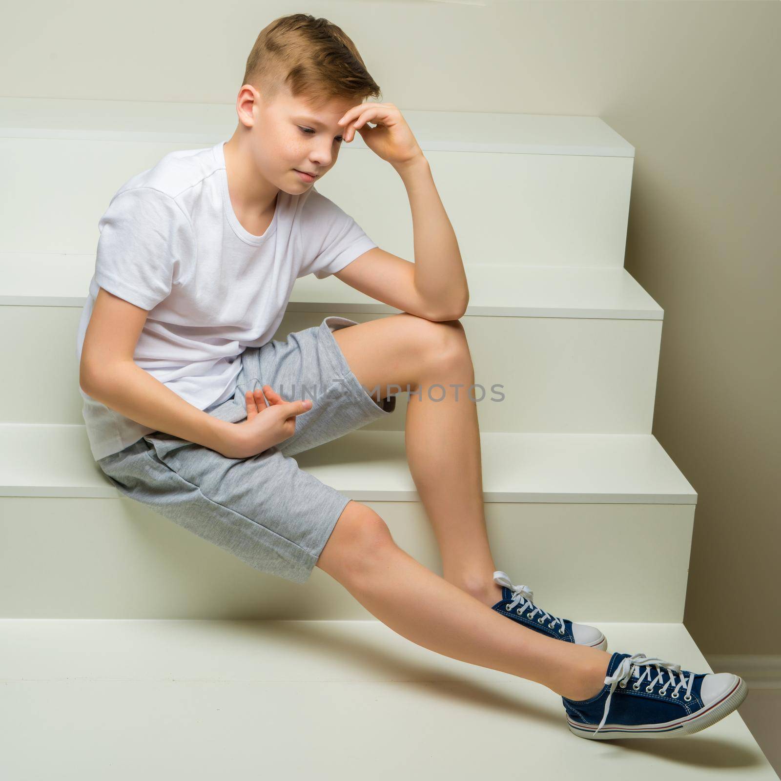 A handsome school-age boy sits on a white staircase. The concept of youth culture.