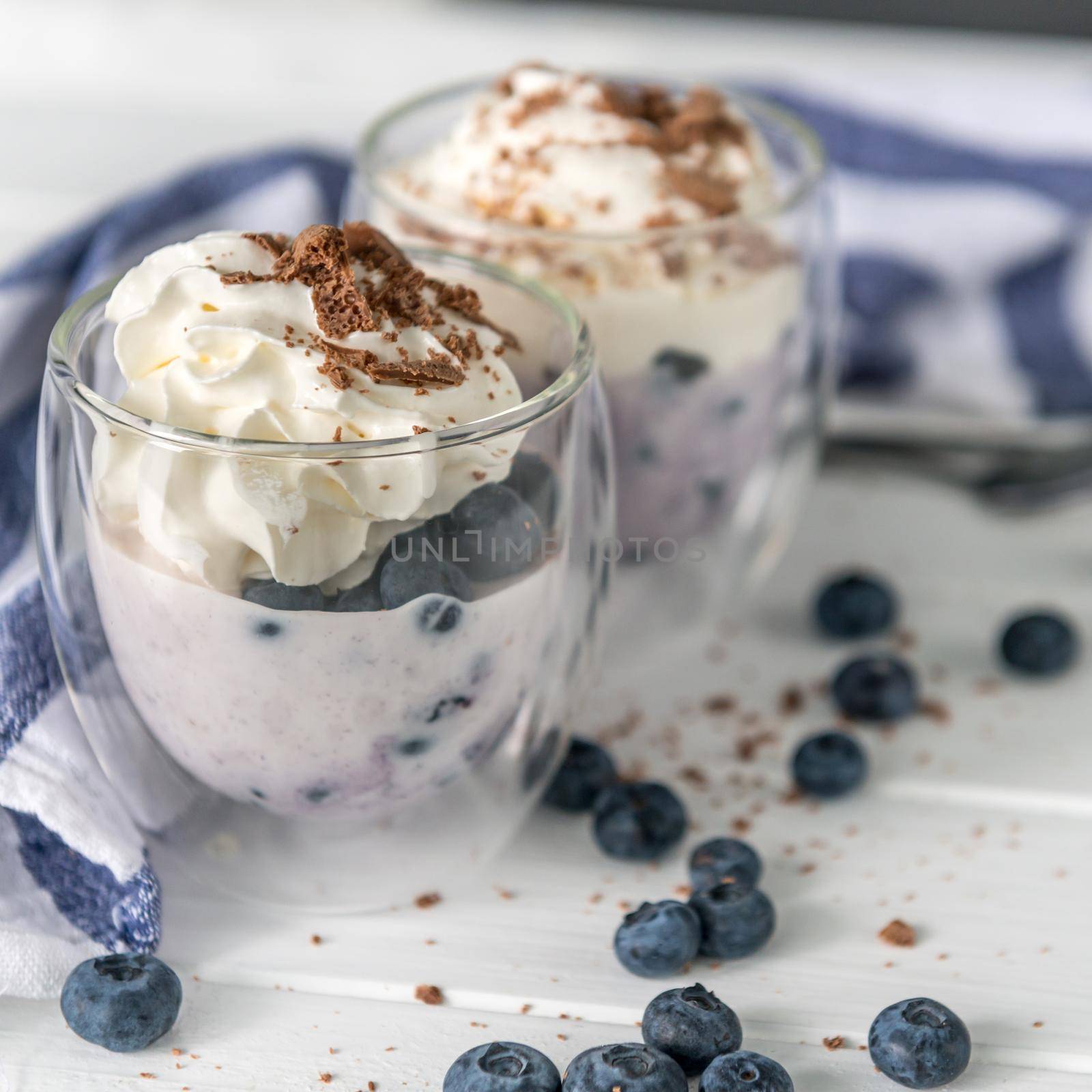 Dessert from yogurt with blueberries and chocolate on a white wooden background