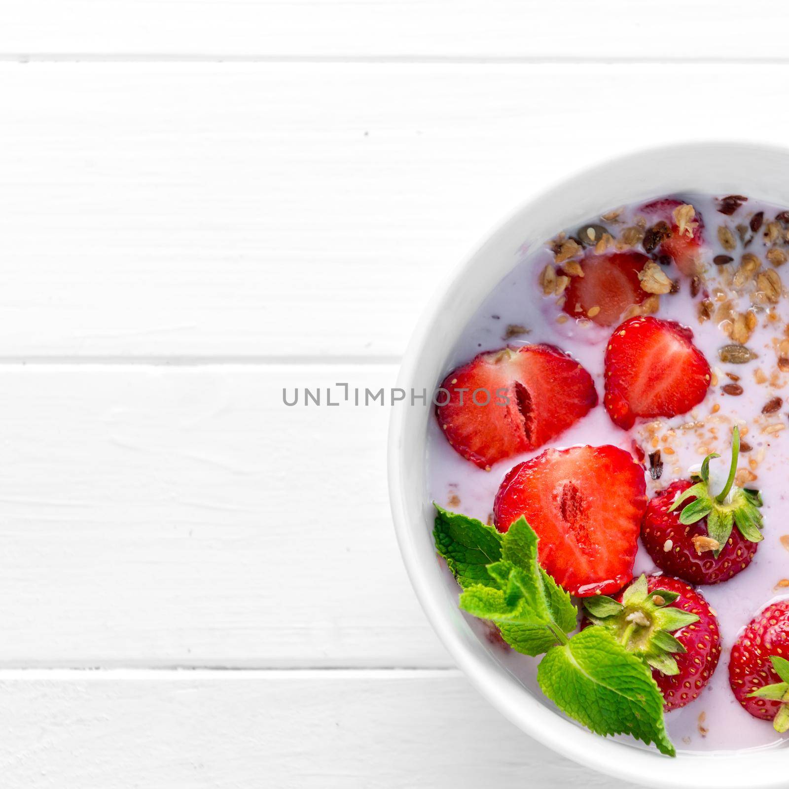 Huge bowl of granola with strawberries and mint leaves, additional textspace left on side, topview