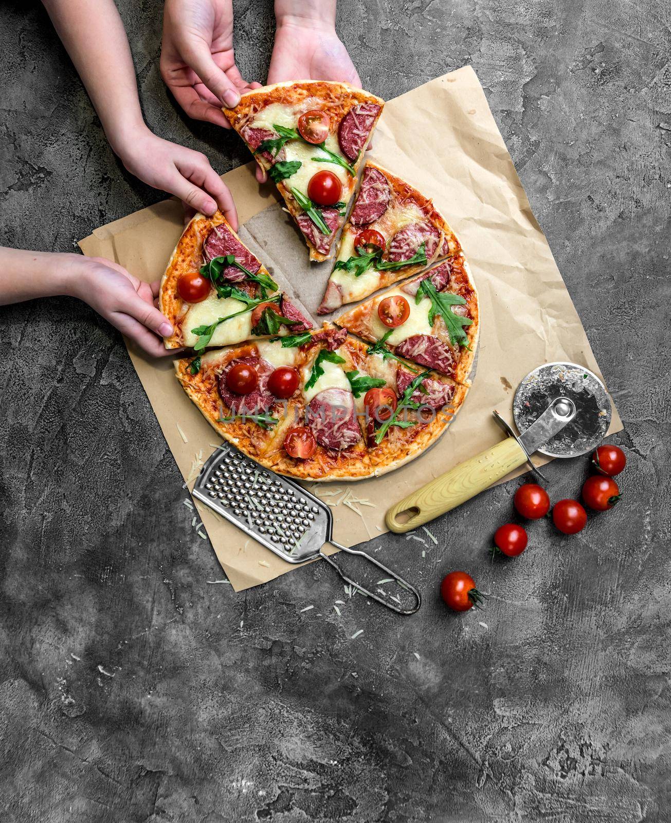 children's hands take homemade pizza with salami, cherry tomatoes and rucola