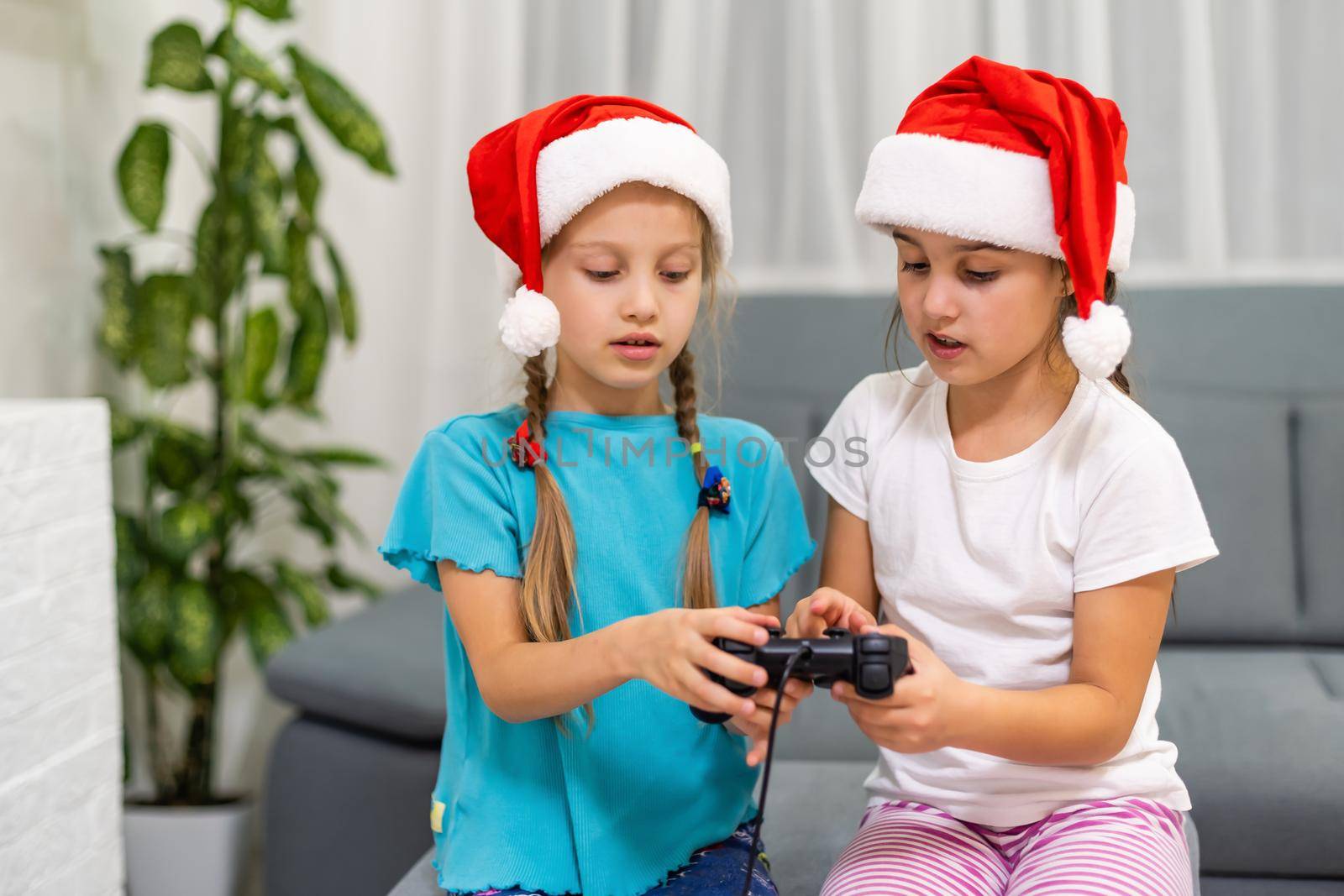Two girls little sister play fun in a video game with a joystick in their hands by Andelov13