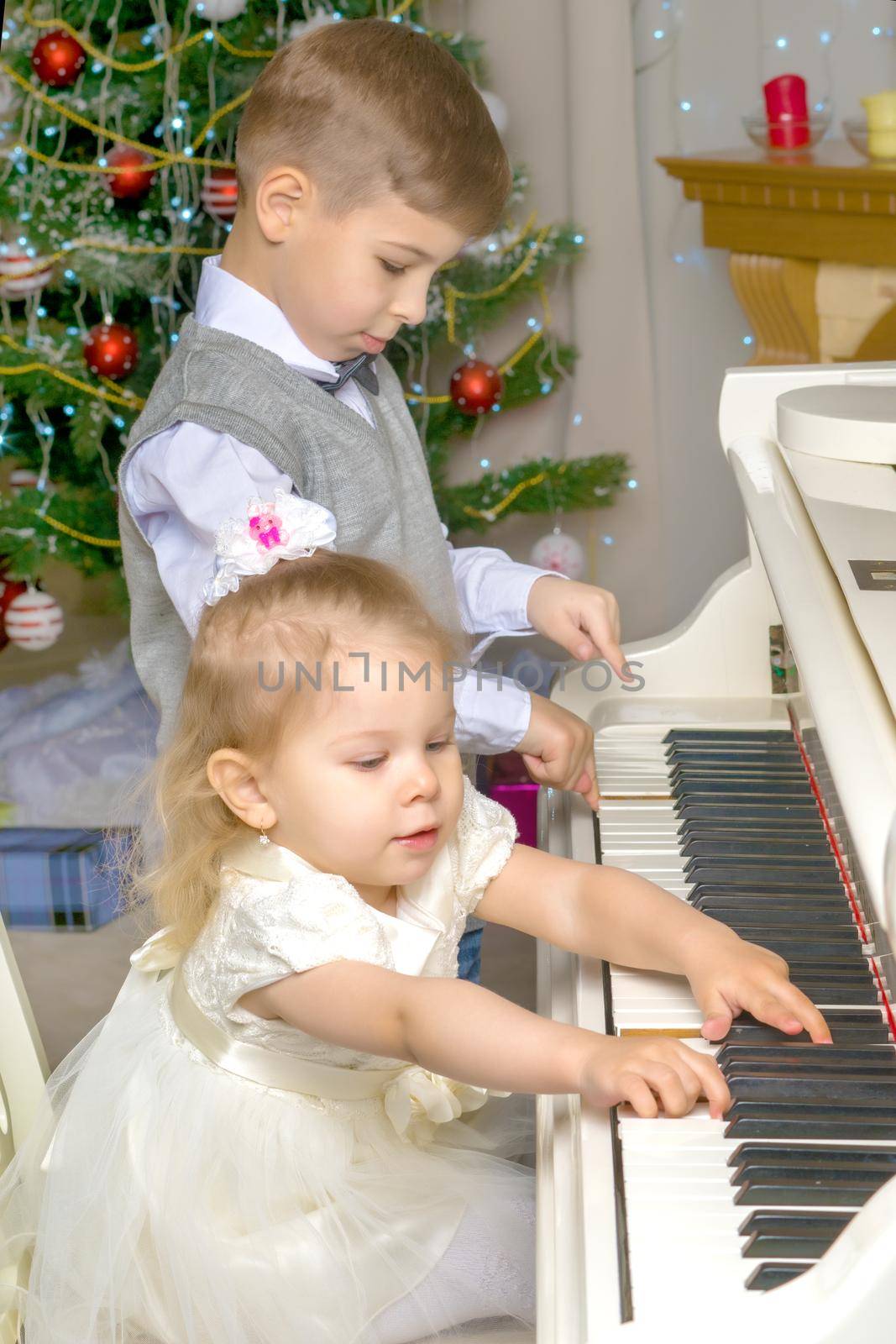 Brother and sister play the piano on Christmas Eve at the Christmas tree. The concept of a holiday, a happy childhood.
