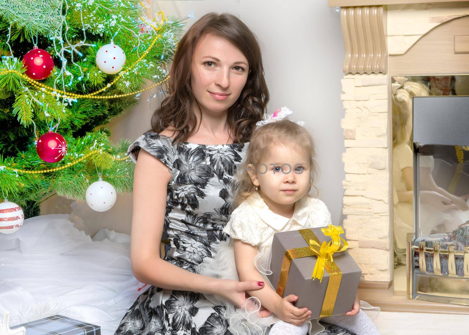 Happy young mother with her little daughter, on Christmas Eve near the Christmas tree with gifts and toys. The concept of holidays and happy childhood.