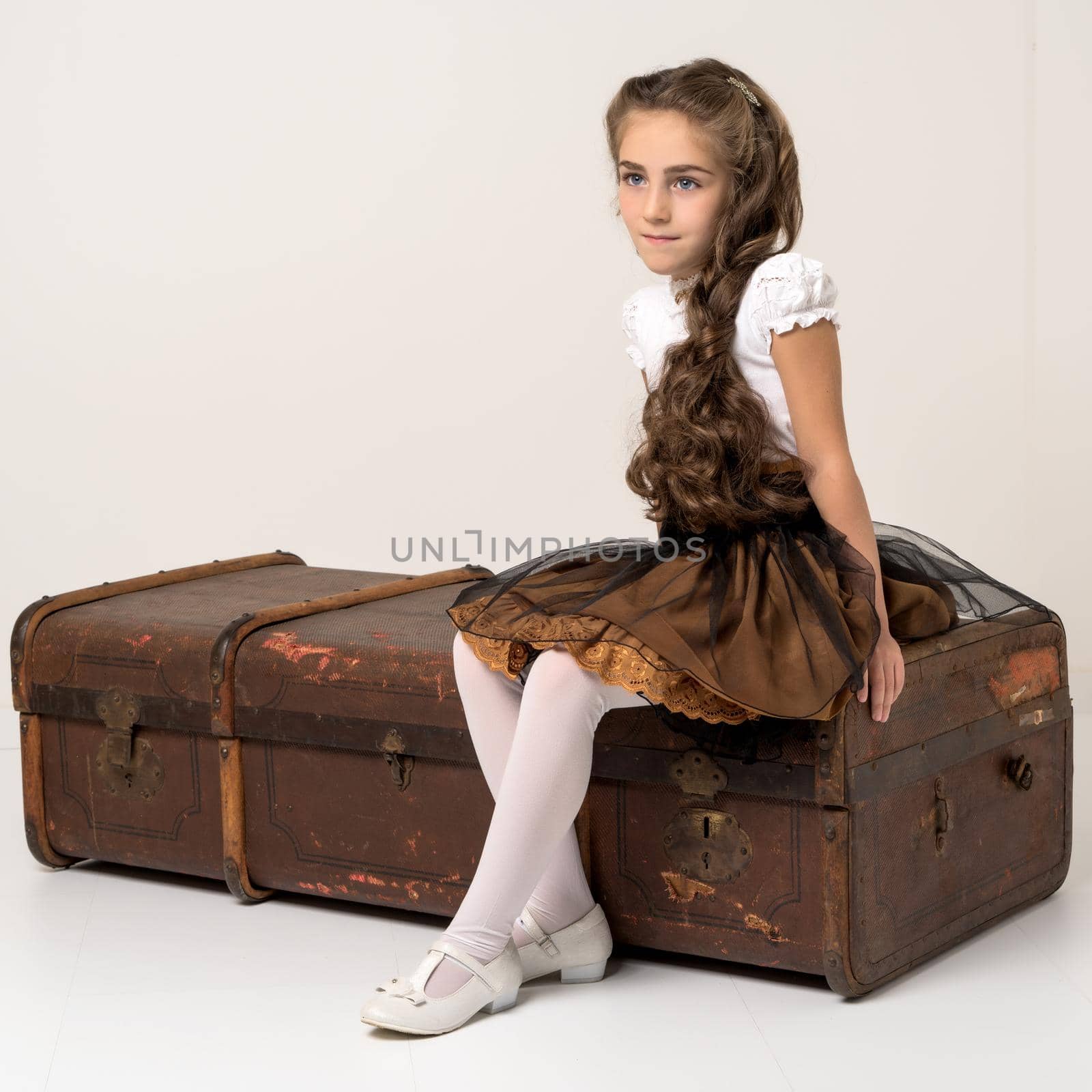 Little girl is sitting on a wooden box. Isolated on white background.