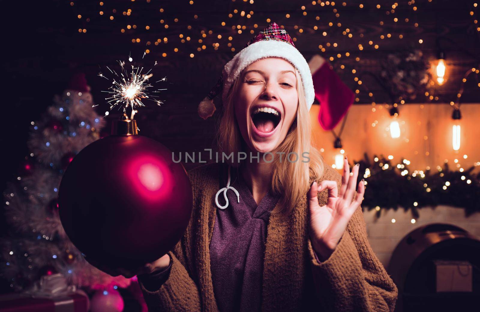 Christmas woman hold bomb. Crazy merry Christmas and Happy New Year. Crazy comical face. Young funny woman wink. Comic grimace. Bomb emotions. by Tverdokhlib