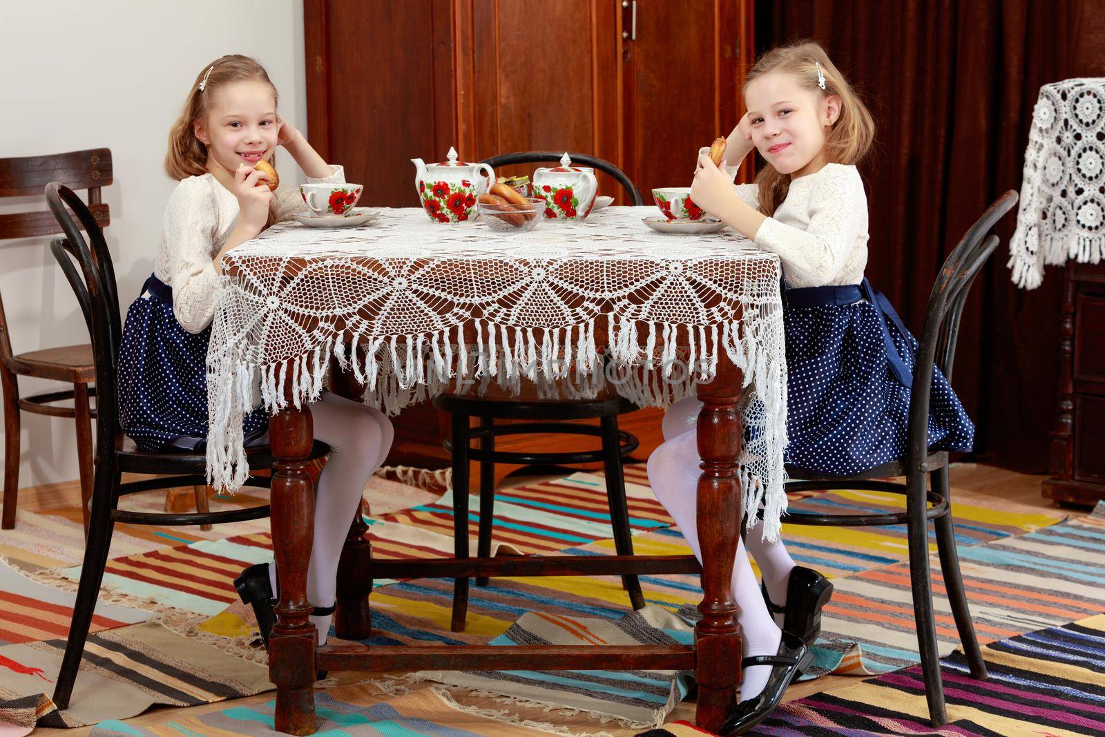 Cute little girls twins drinking tea at an antique table with a lace tablecloth.Retro style.