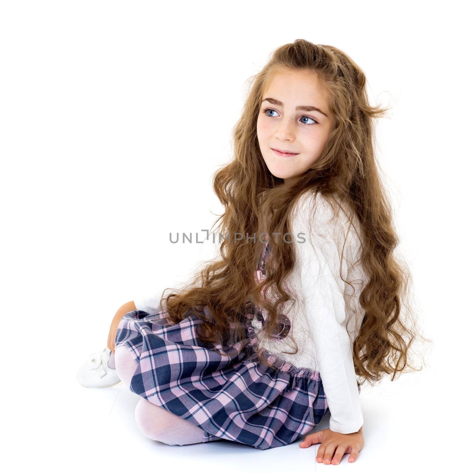 Beautiful little girl kneels in the studio on a white background. The concept of beauty and fashion, children's emotions. Isolated.