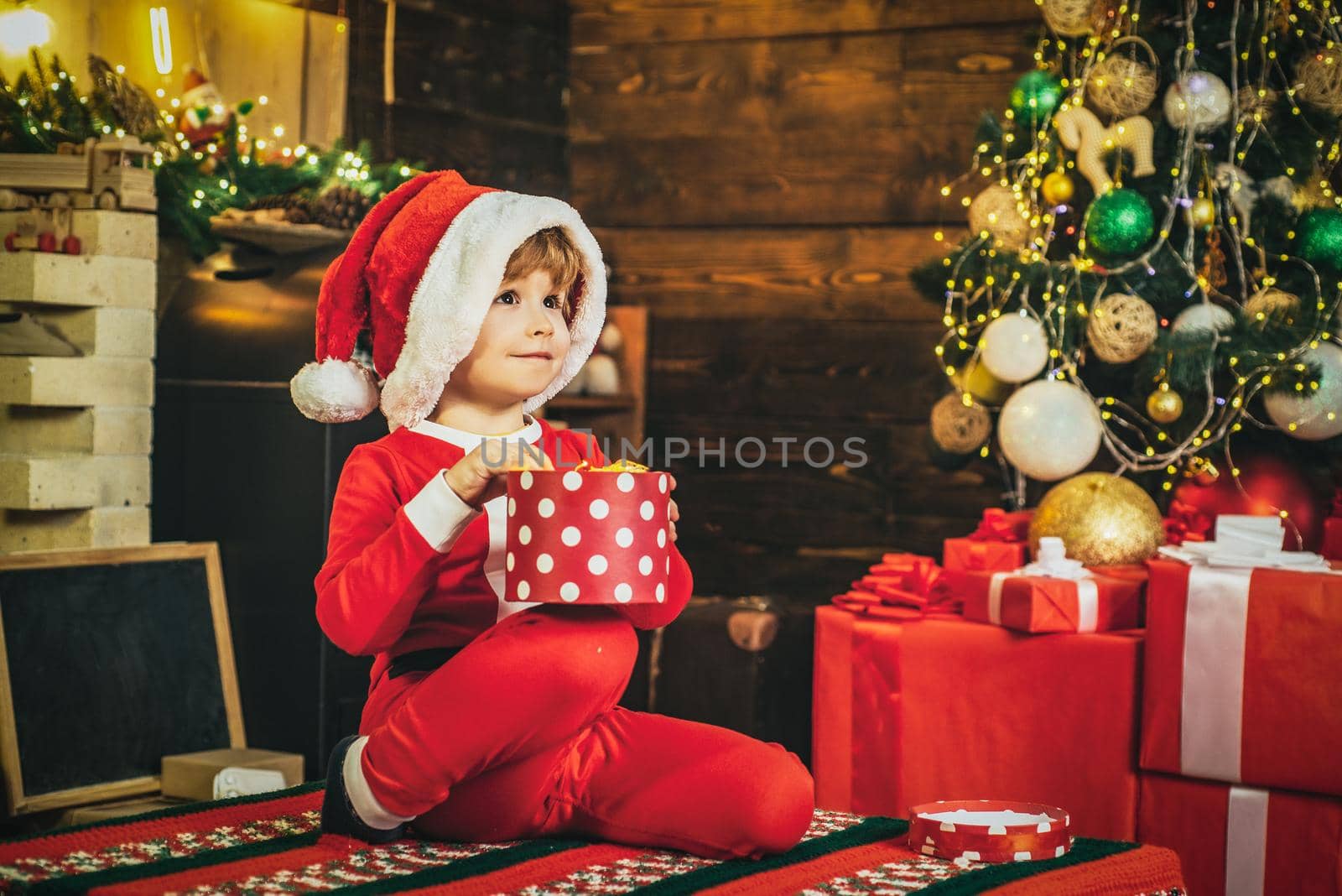 Child dressed in winter clothing think about Santa near Christmas tree. Merry Christmas for kids