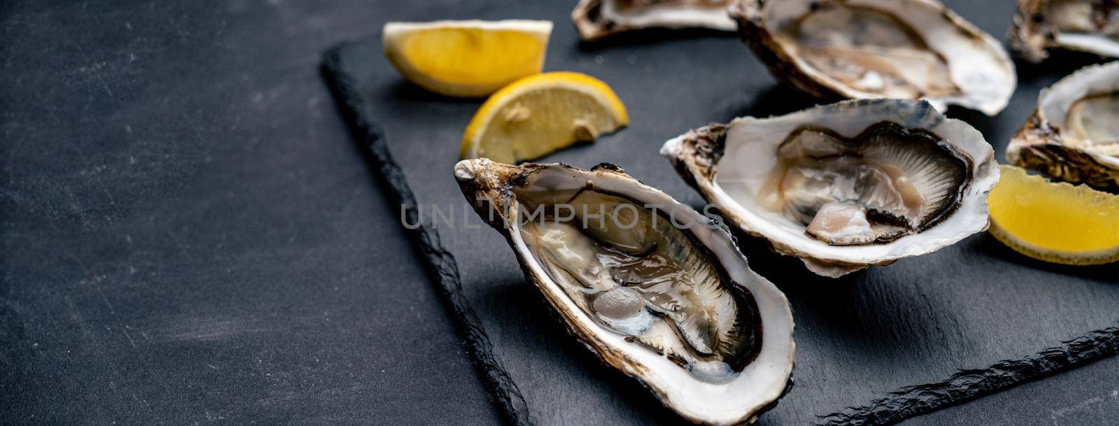 Fresh oysters with lemon served on balck platter. Luxury seafood diet