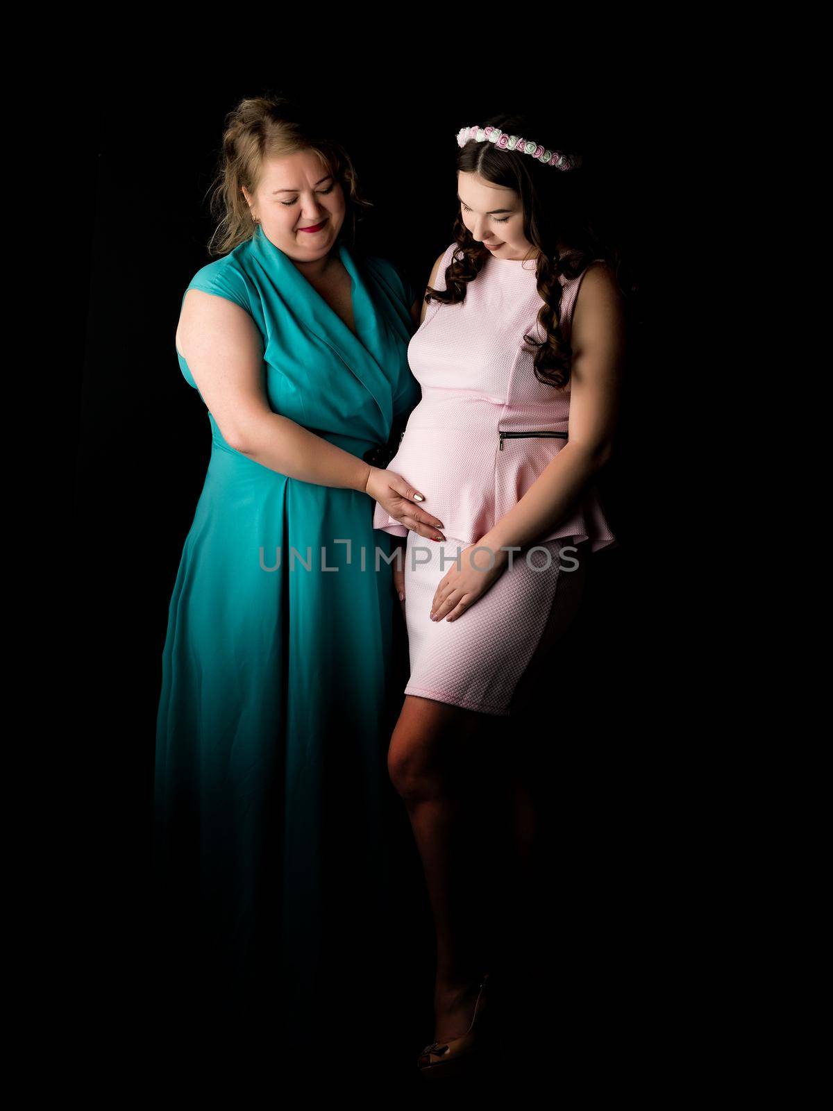 Young pregnant girl with mother on a black background.