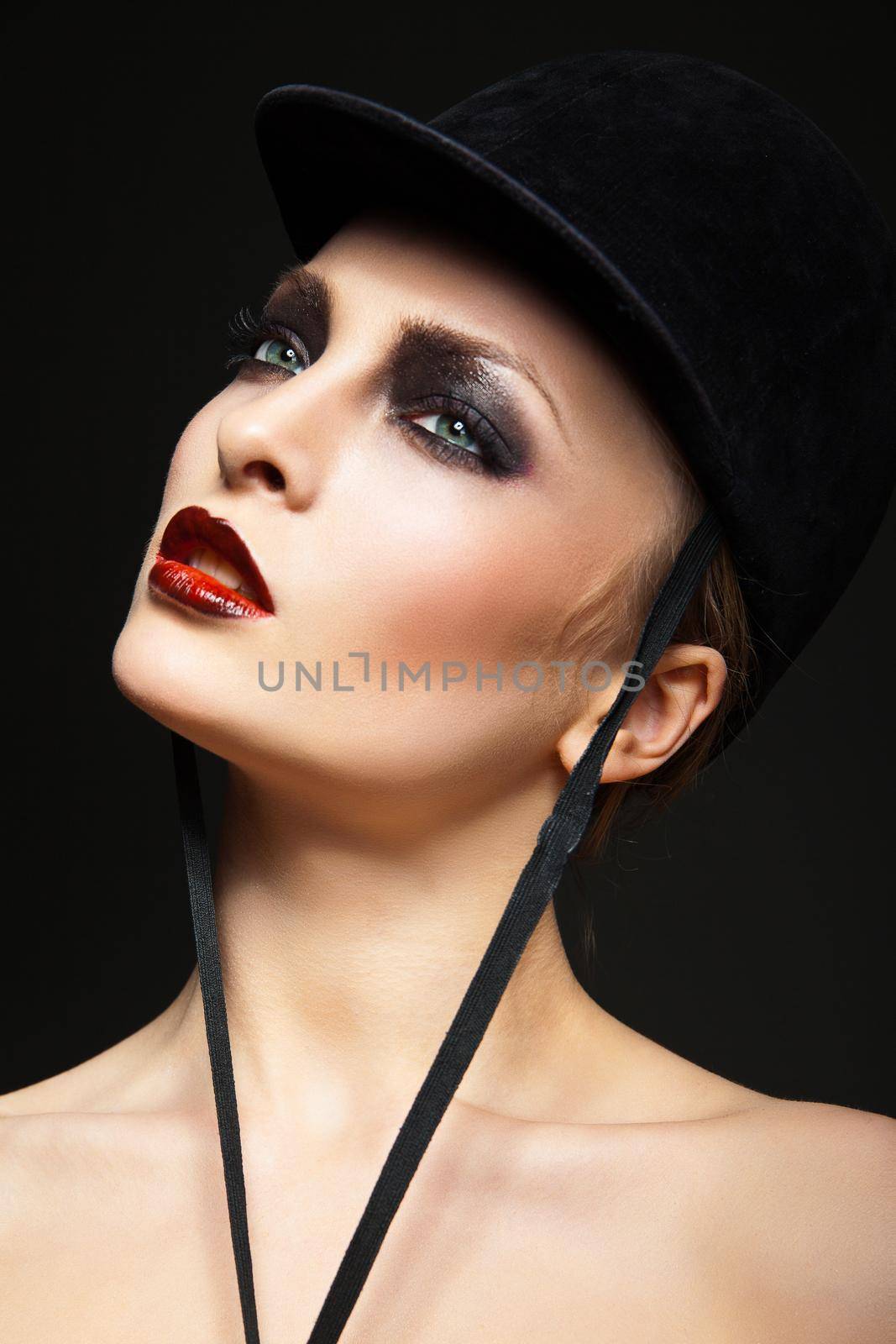 Blond fashion horsewoman wearing hat posing over black background