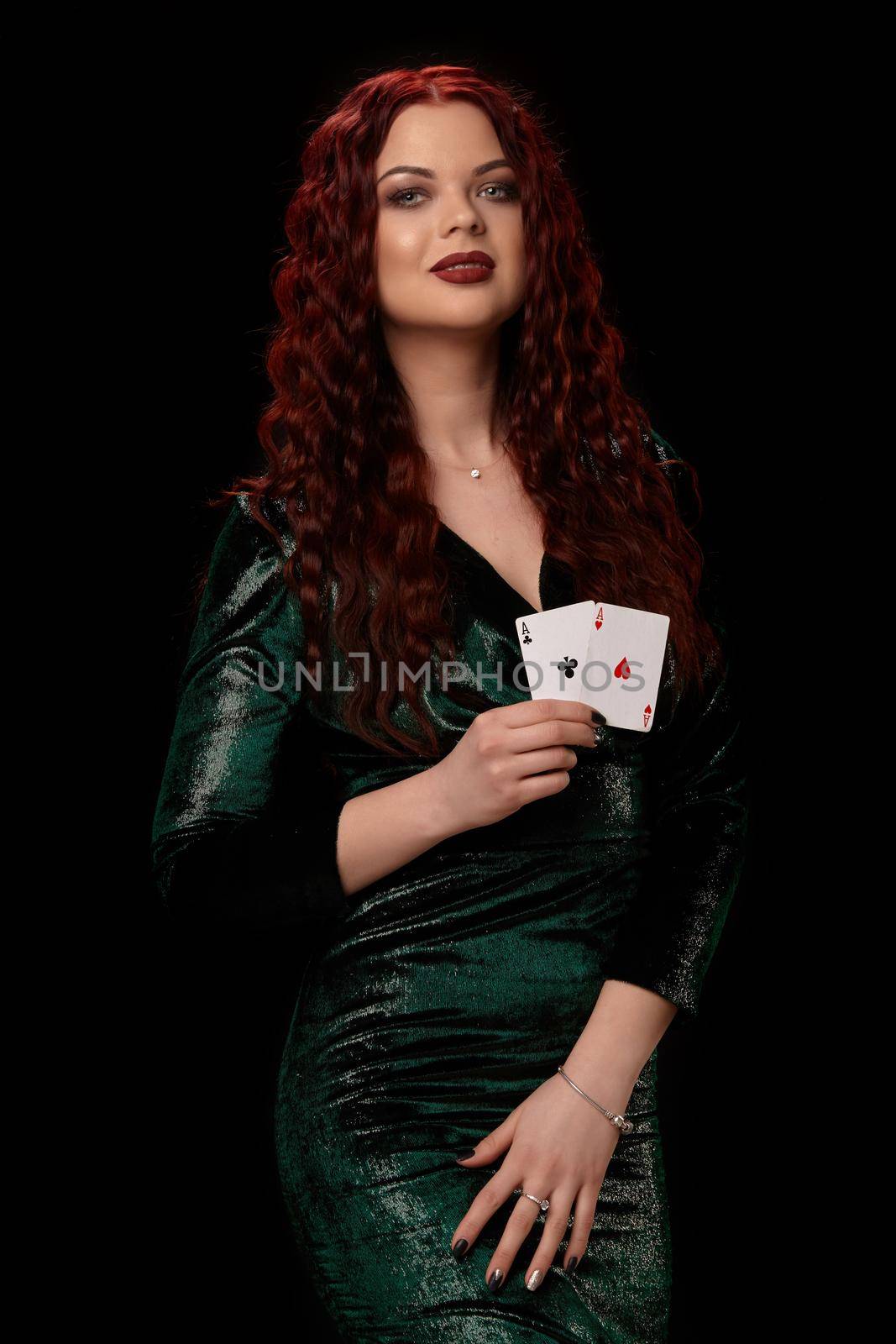 Redheaded woman whith a curly hair and red lipstick on her lips, smiling with playing cards in her hands, on black background Win casino poker slots