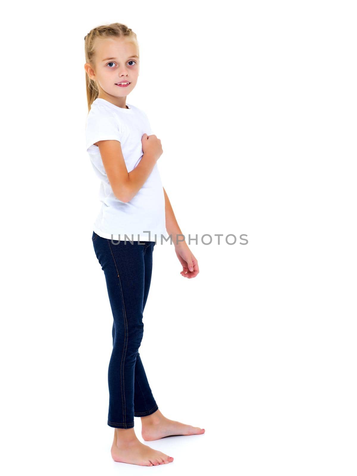 A beautiful little girl in an empty white T-shirt points to herself. The concept of design of T-shirts, advertising of children's goods. Isolated on white background.