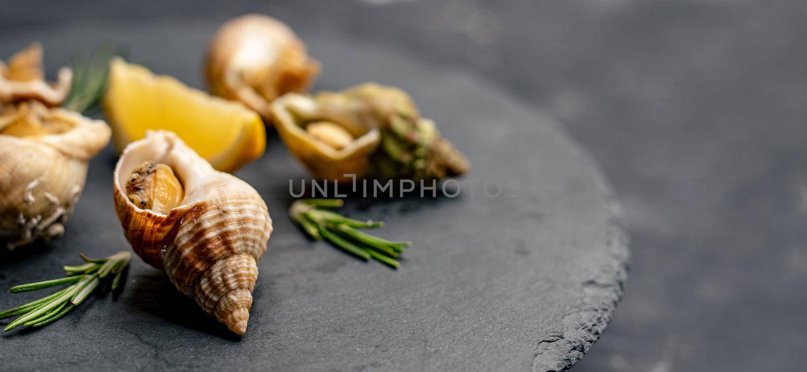 Cooked french snails served with lemon and rosmarine on black round platter