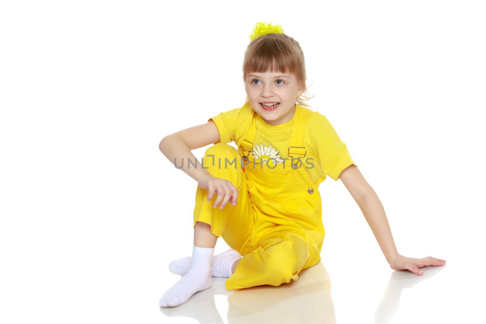 Girl with a short bangs on her head and bright yellow overalls.She crouched down on the white advertising banner.