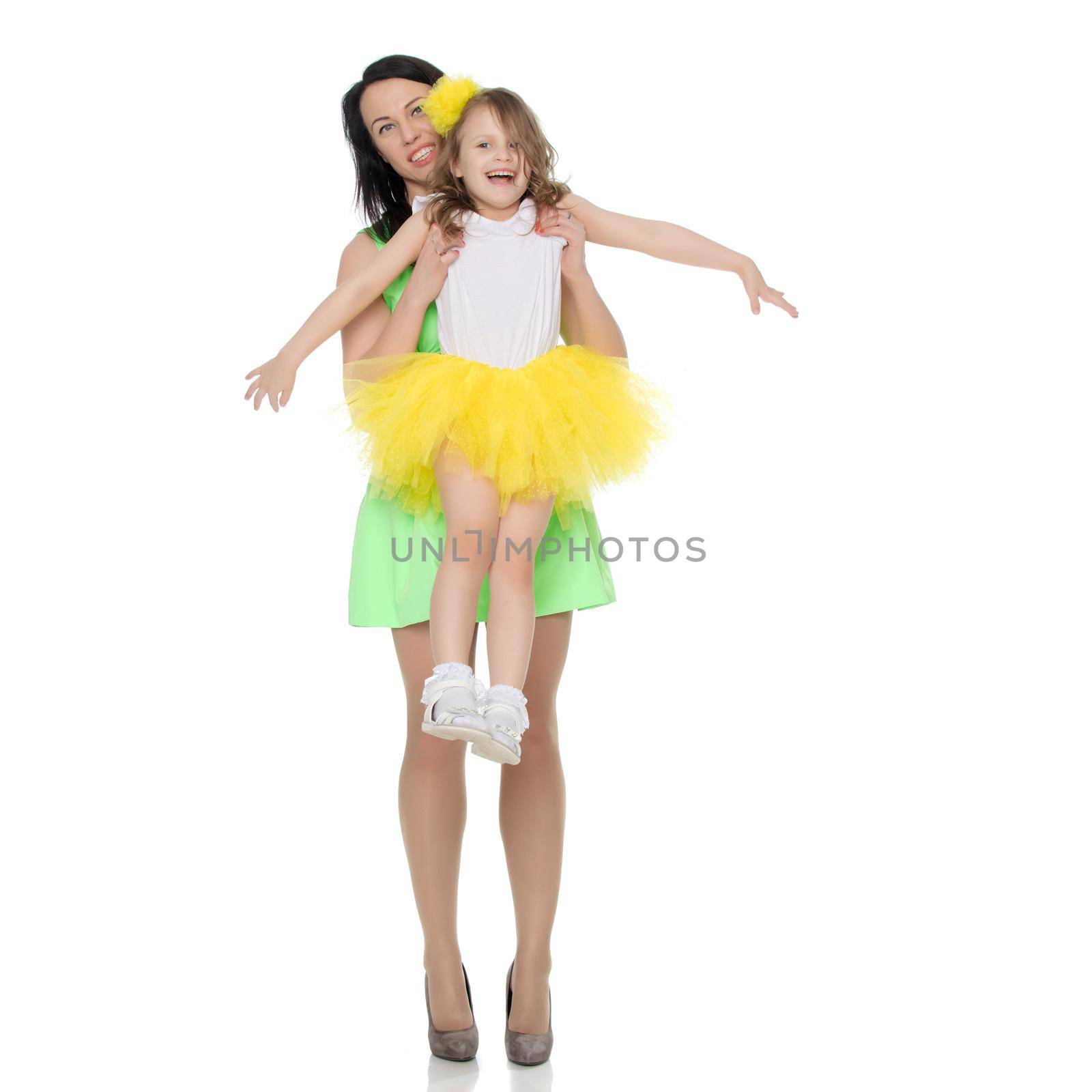 Beautiful young mother in a short green dress and her little beloved daughter in a yellow skirt.Fun mother throws daughter on hands.Isolated on white background.