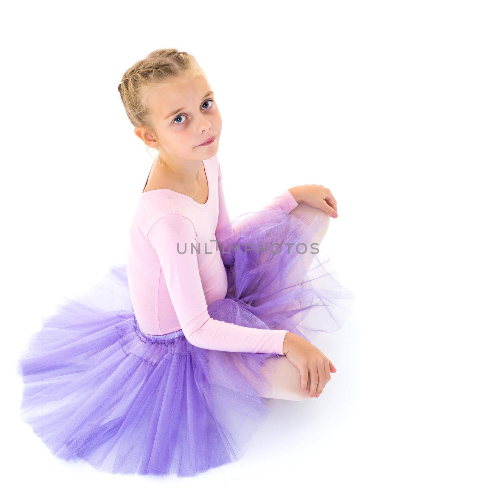 Charming little girl ballet dancer performing ballet poses on the floor in the studio on a white background.Isolated.