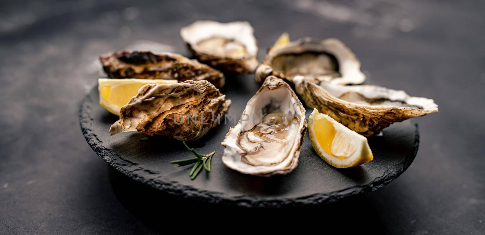 Beautiful picture of delicatessen oysters served with lemon on black round platter