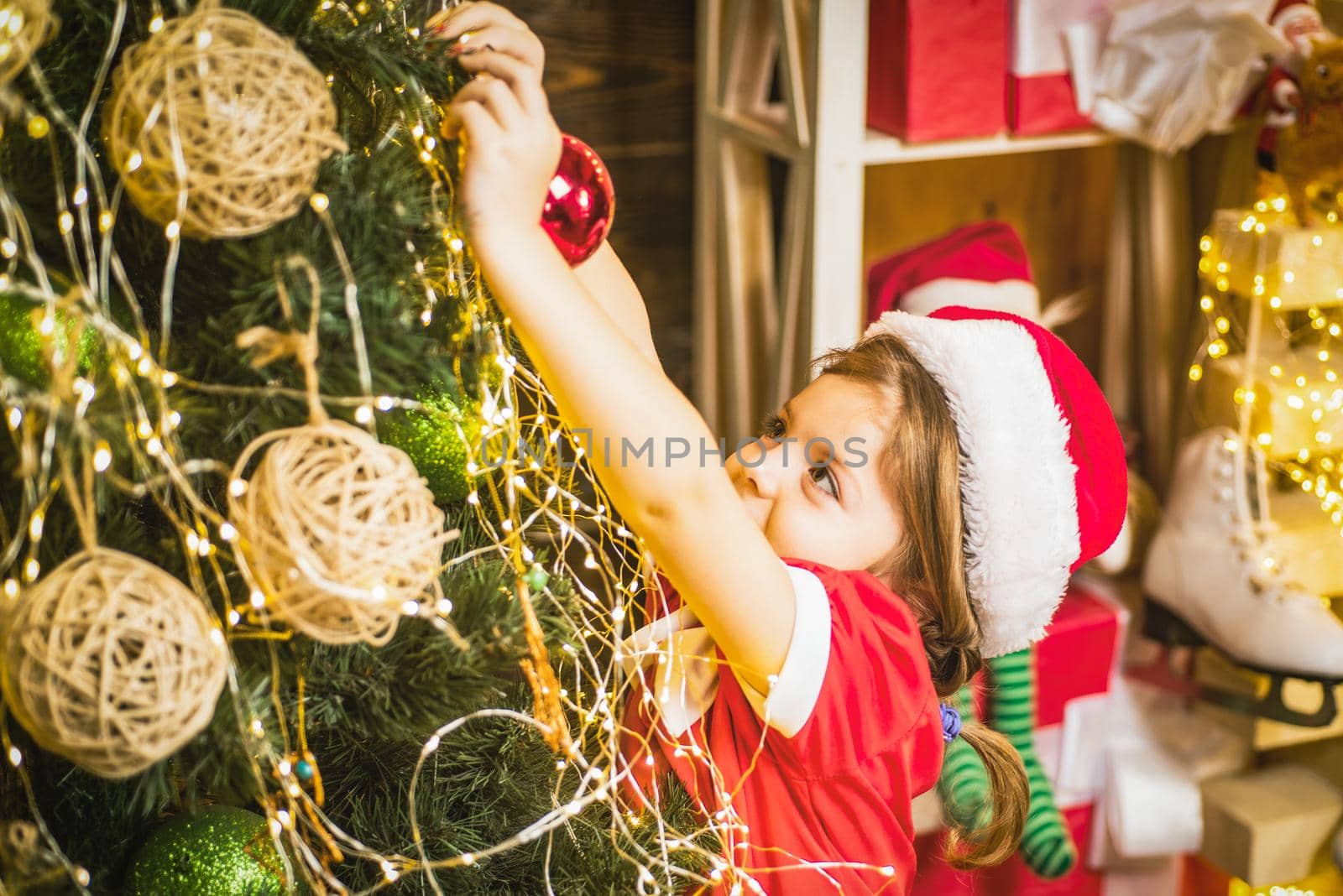 Cute child girl is decorating the Christmas tree. Kid decorating Christmas tree with bauble. by Tverdokhlib