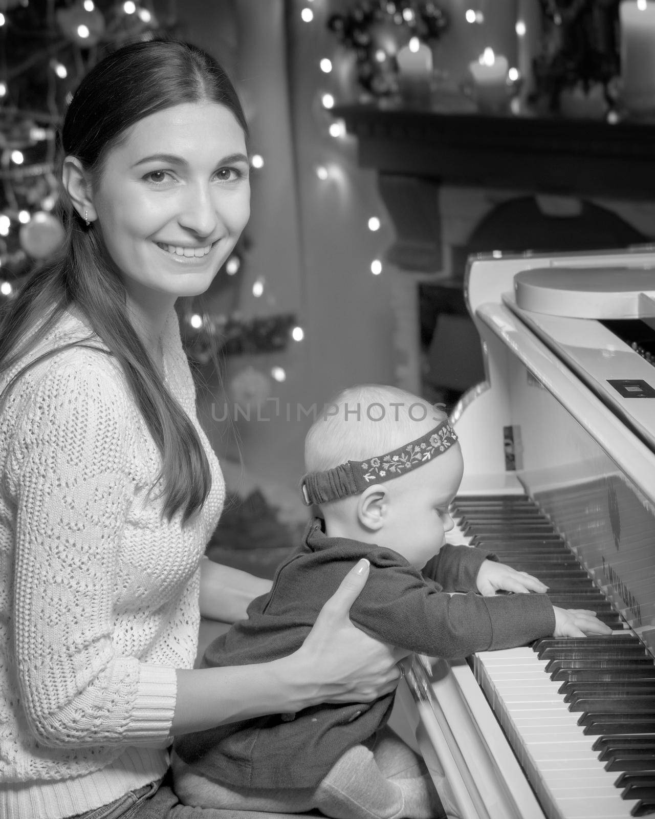 A young mother with a small child on Christmas night with candles near a large white piano. The concept of holidays and family happiness.