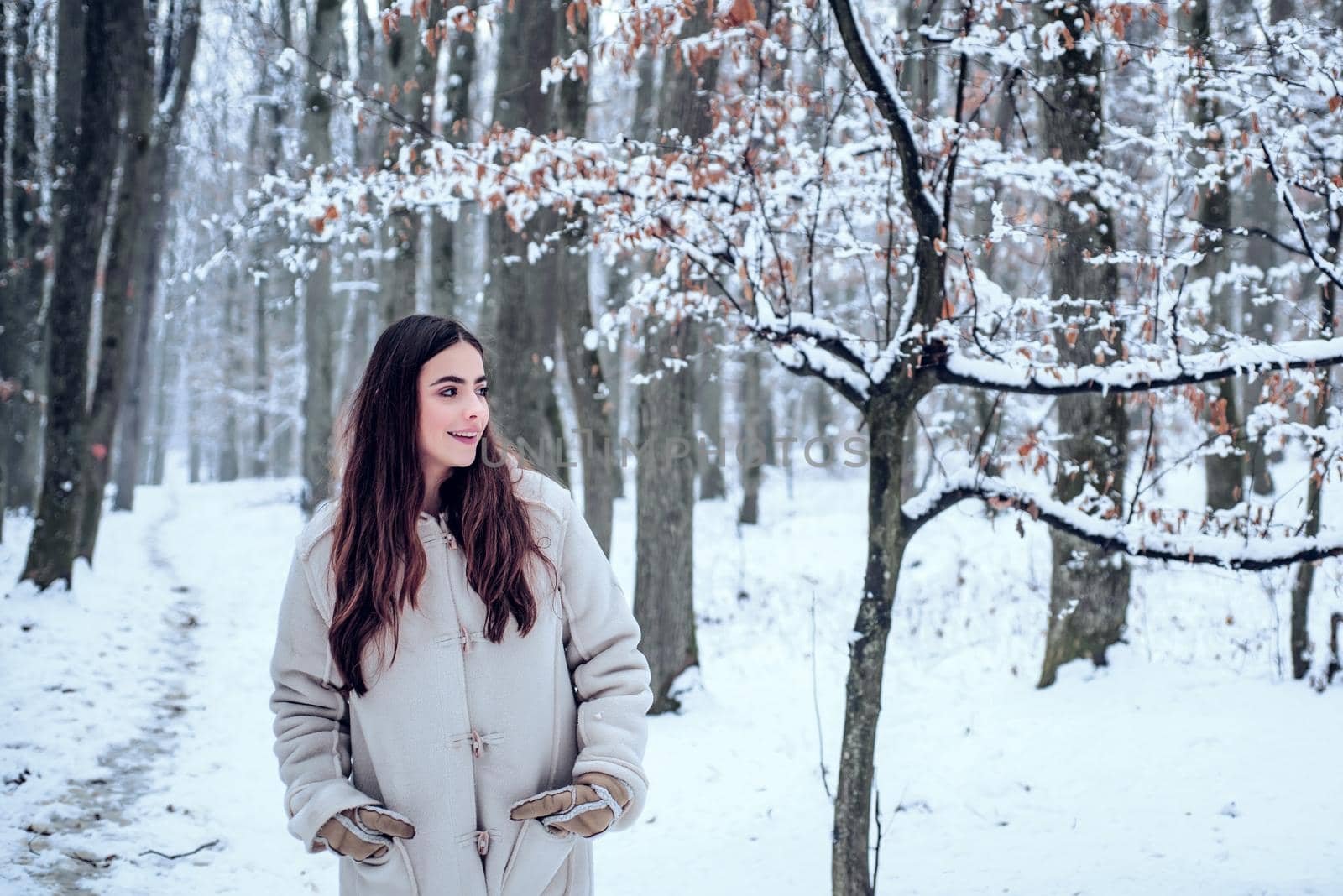 Winter woman. Portrait of a young woman in snow trying to warm herself. Beautiful girl in the winter forest in white down jacket