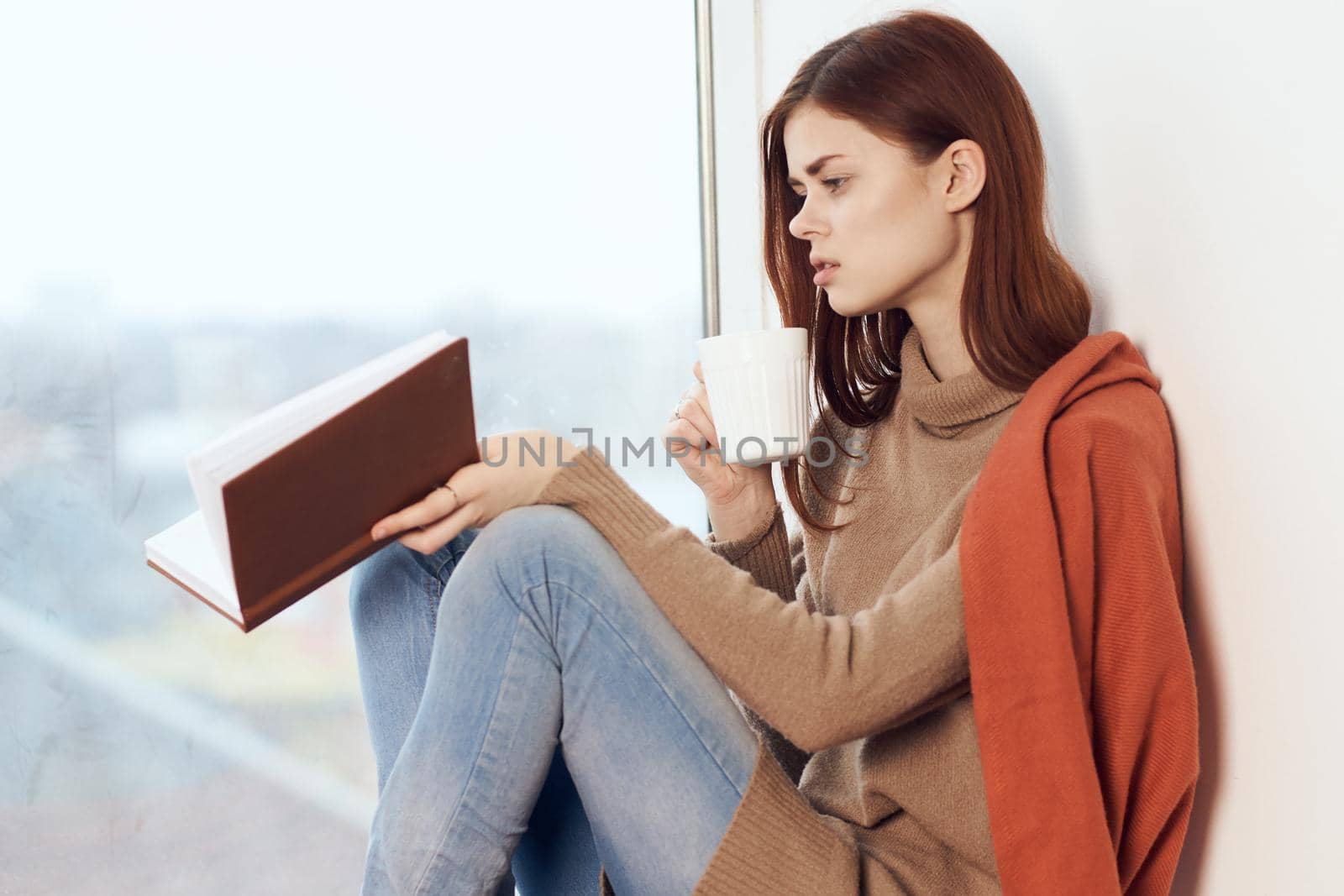 woman with a book near the window with a cup of coffee by Vichizh