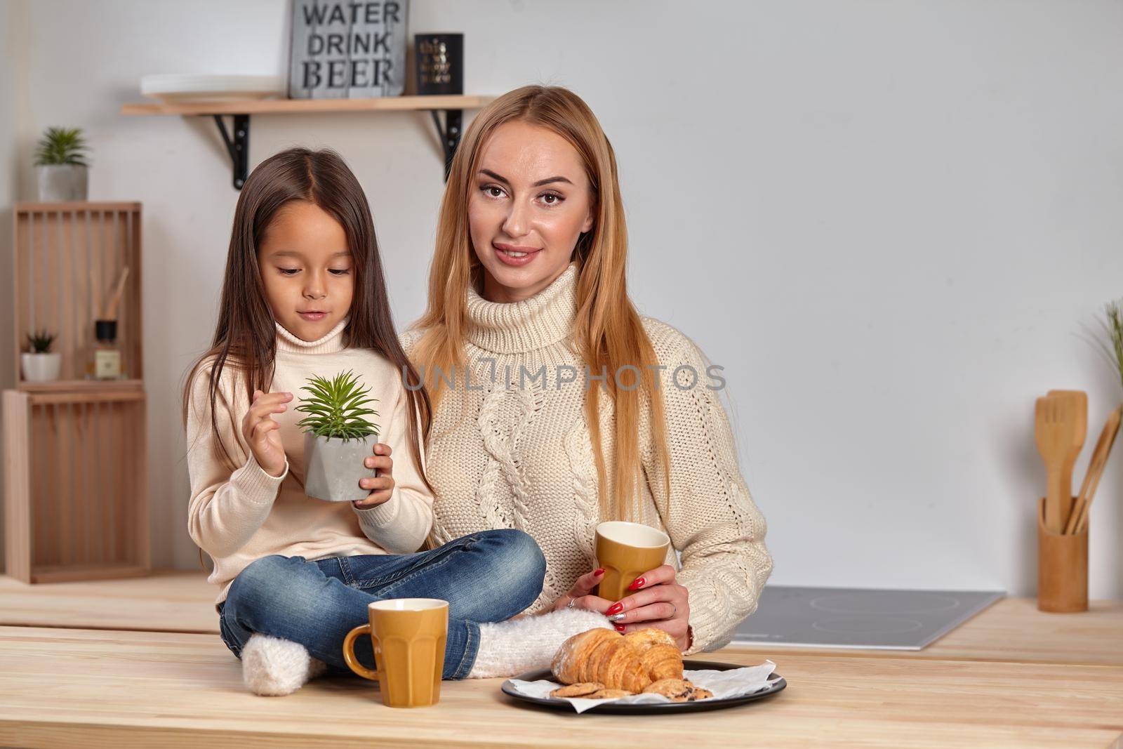 Caring mom. Nice smiling mother giving croissant to her child sitting on the kitchen