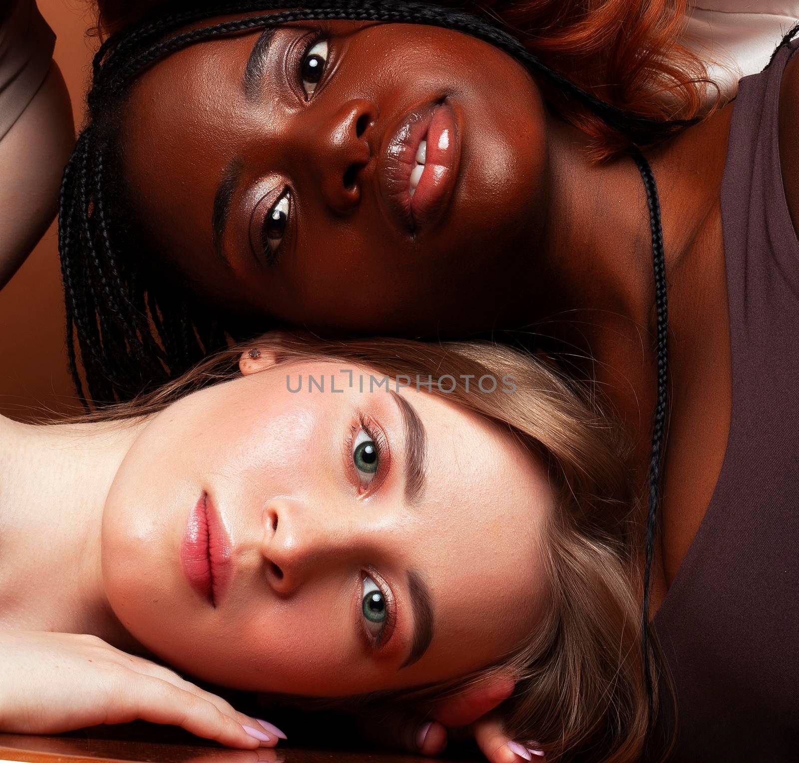 young pretty african and caucasian women posing cheerful together on brown background, lifestyle diverse nationality people concept close up