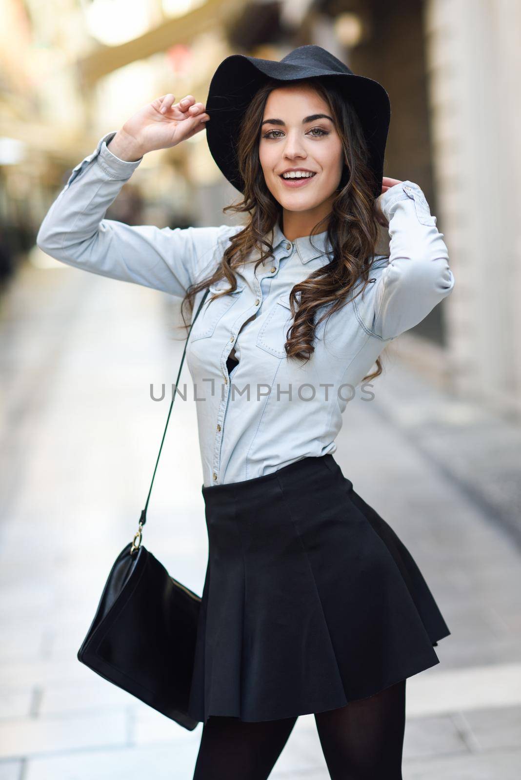Portrait of young woman in urban background wearing casual clothes and hat carrying a bag