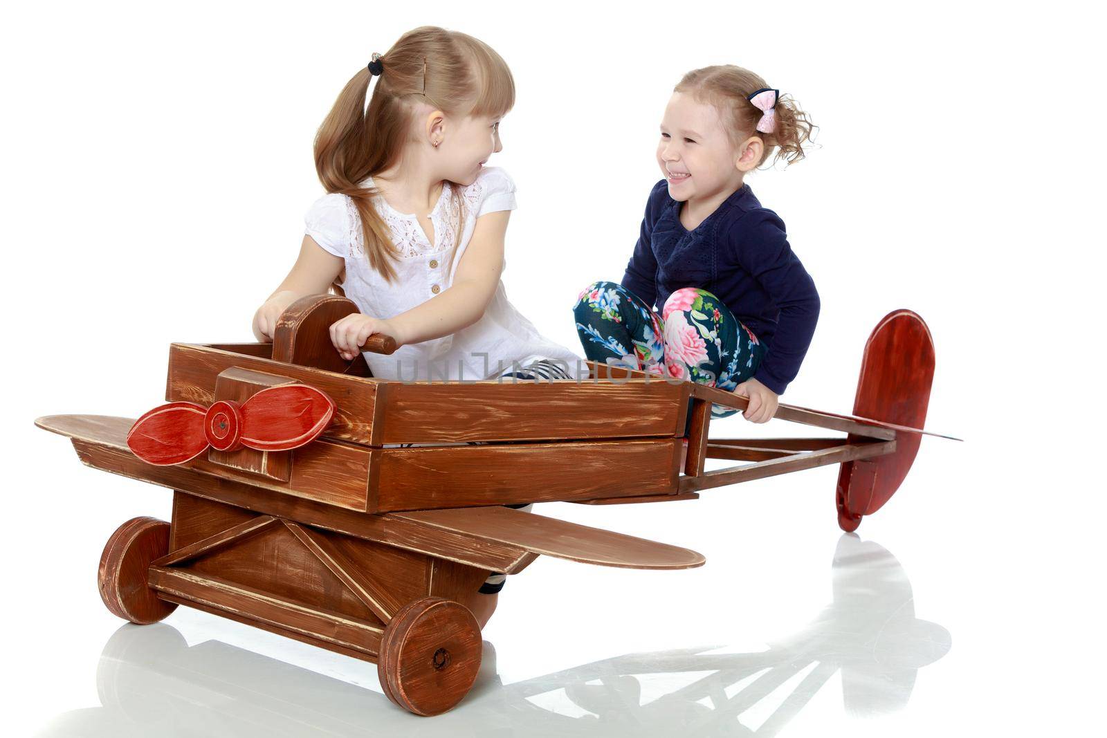 Two girls sister play with a wooden plane. The concept of a happy childhood, playing in the family. Isolated on white background.