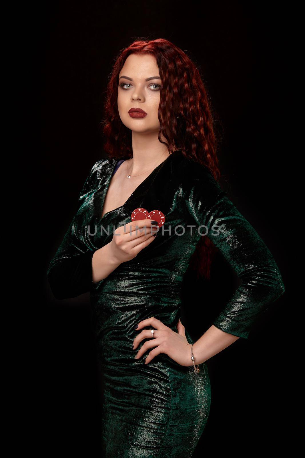 Gorgeous redheaded woman in a black dress turned sideways with chips in her hands, over black. Win casino holdem poker slots