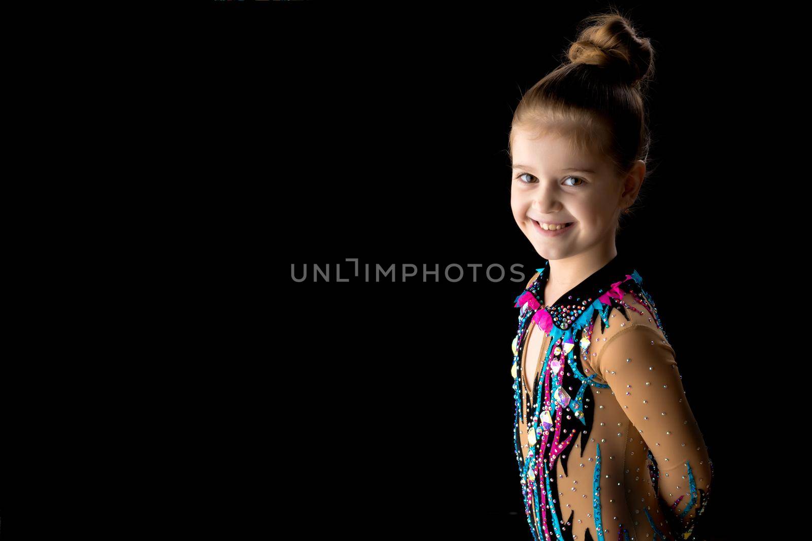 Beautiful little girl gymnast in a sports swimsuit on a black background. The concept of a happy childhood, a healthy lifestyle.