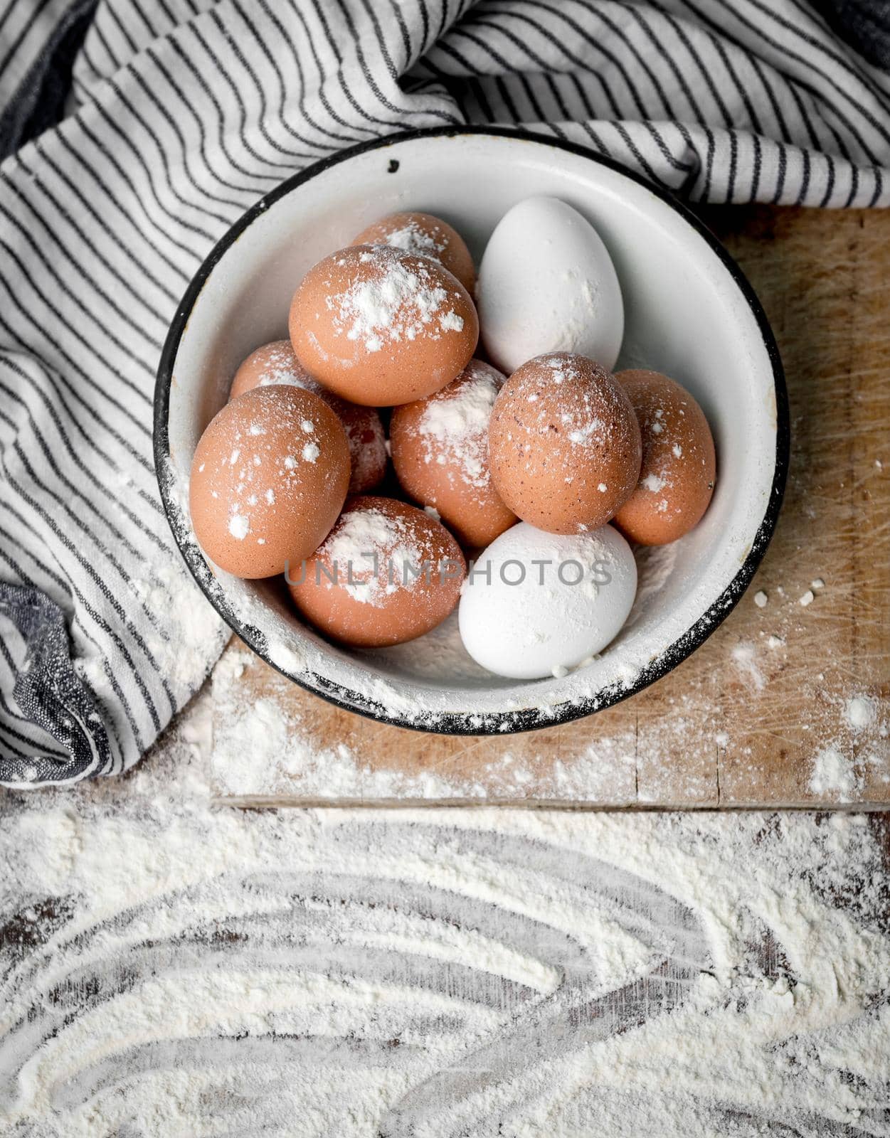 Brown and white fresh eggs sitting in a bowl, table covered with flour, topview