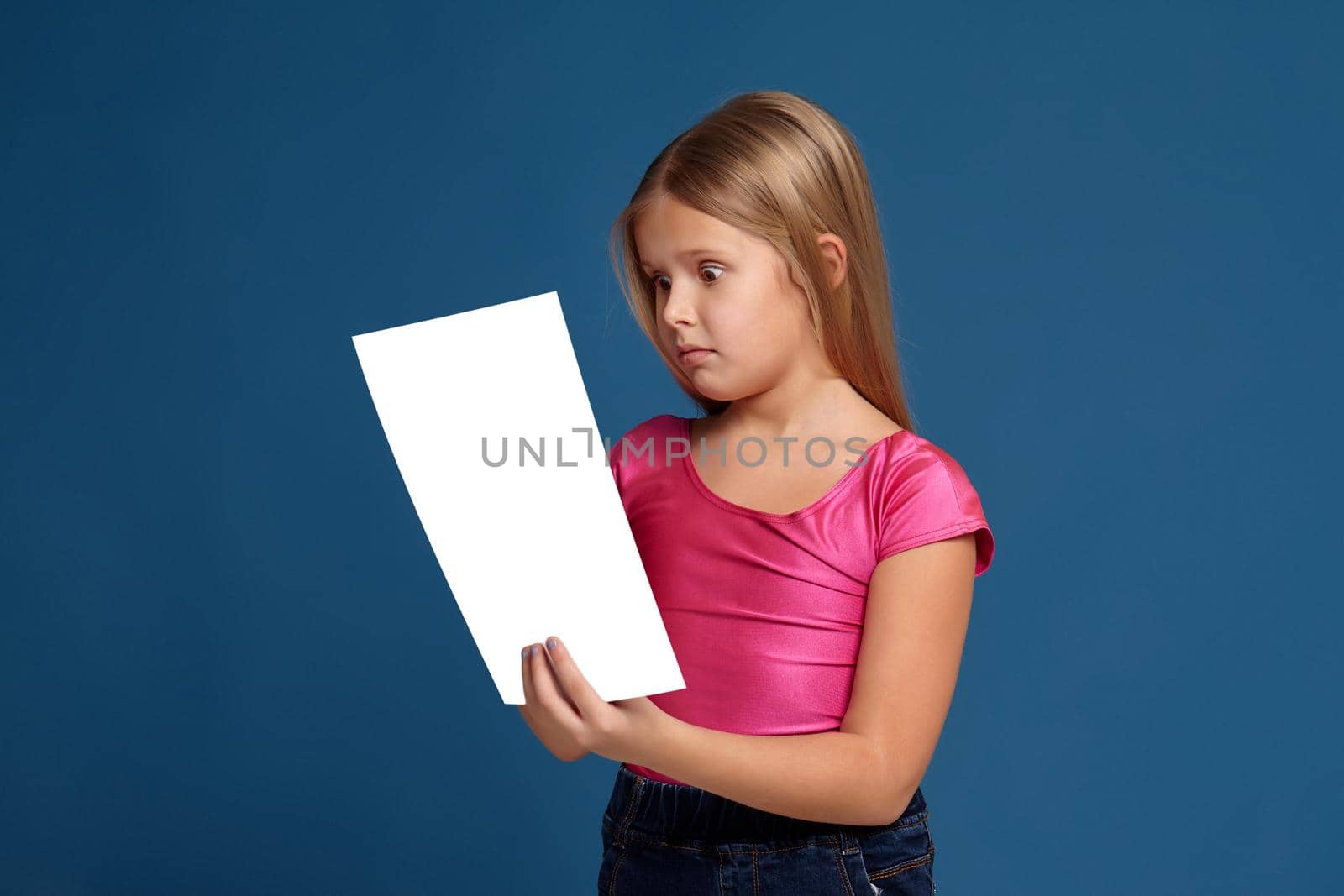Portrait of adorable blonde little girl on blue background. in pink shirt, reading vertical white copy space