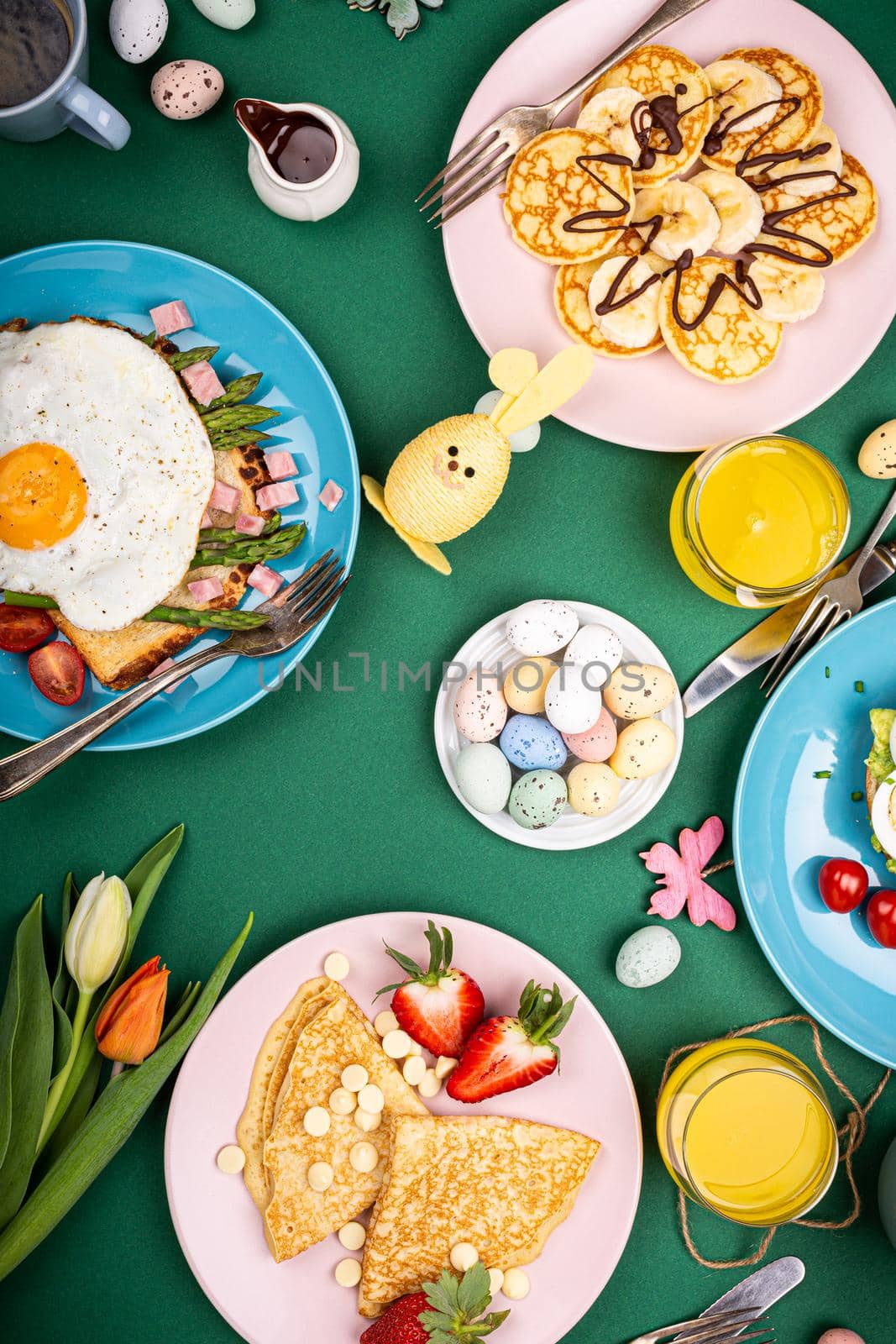 Easter composition with breakfast flat lay with scrambled eggs bagels, tulips, pancakes, bread toast with fried egg and green asparagus, colored quail eggs. Top view.