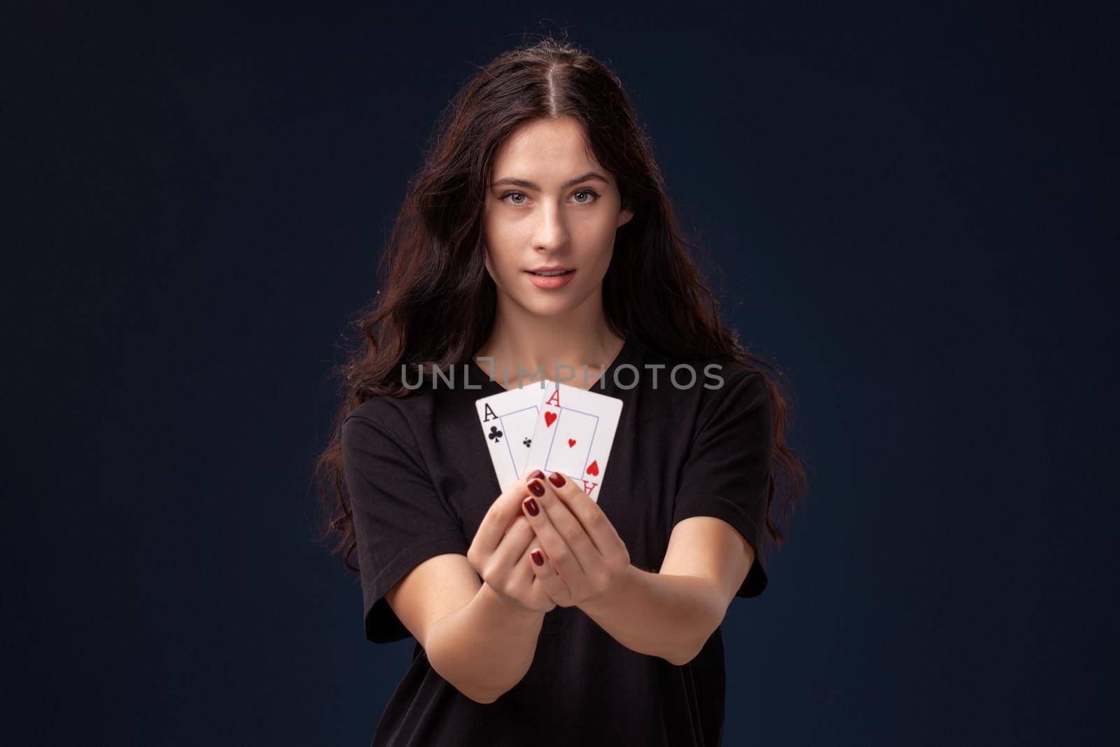 Curly hair brunette wearing a blackish t-shirt is showing playing cards in her hands and looking at the camera. Poker concept on a black background. Casino.