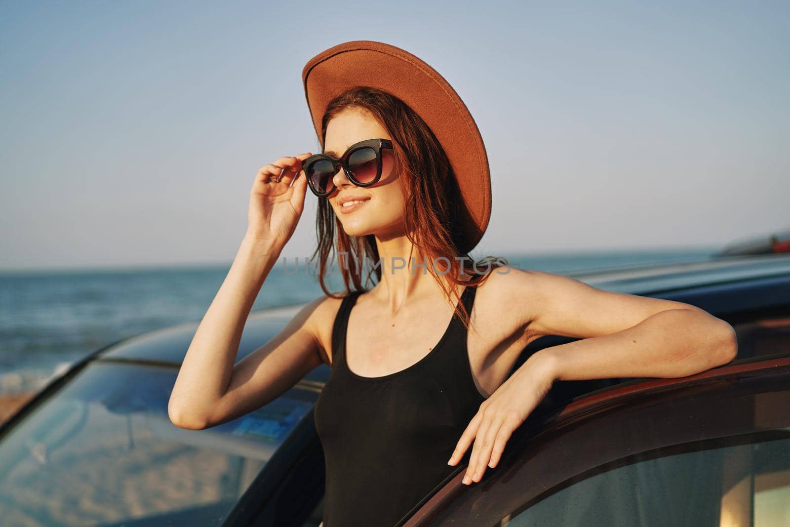 cheerful woman in sunglasses and a hat on the ocean near the car. High quality photo