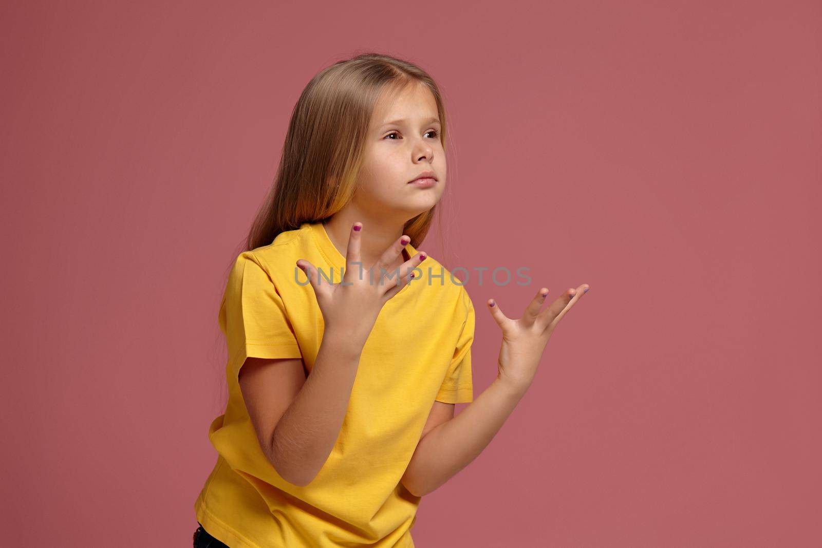 little girl in a yellow t-shirt on coral background. surprised shows hands