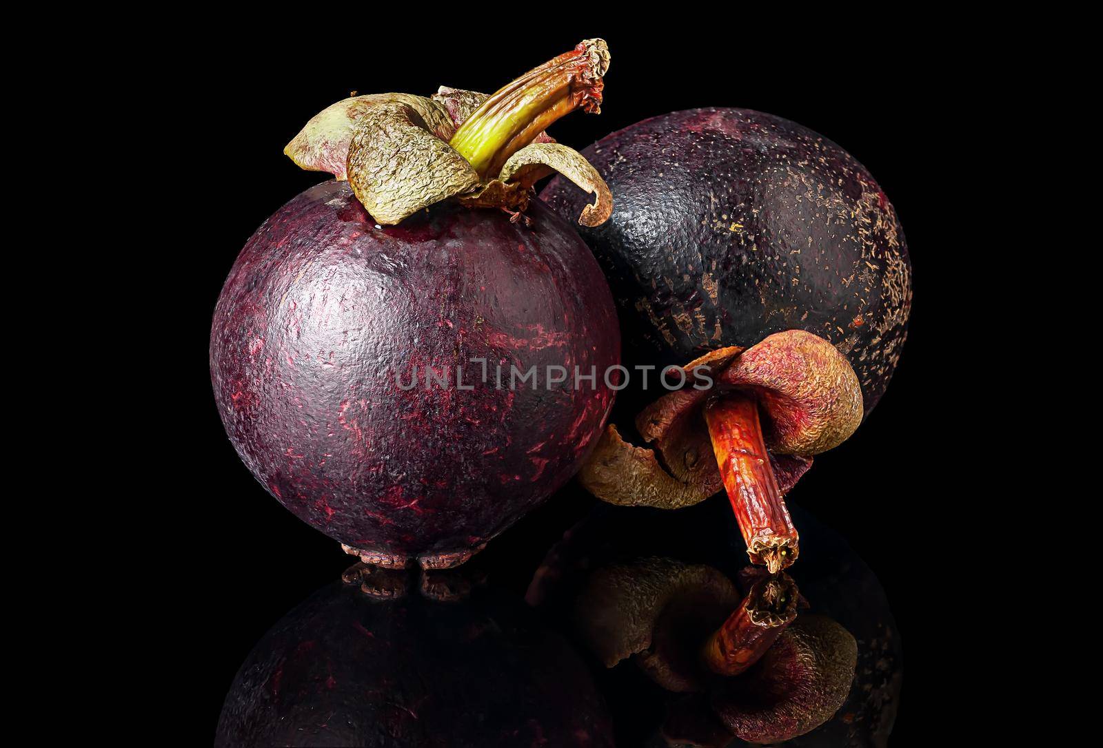 Two ripe mangosteen one after another on a black by Cipariss