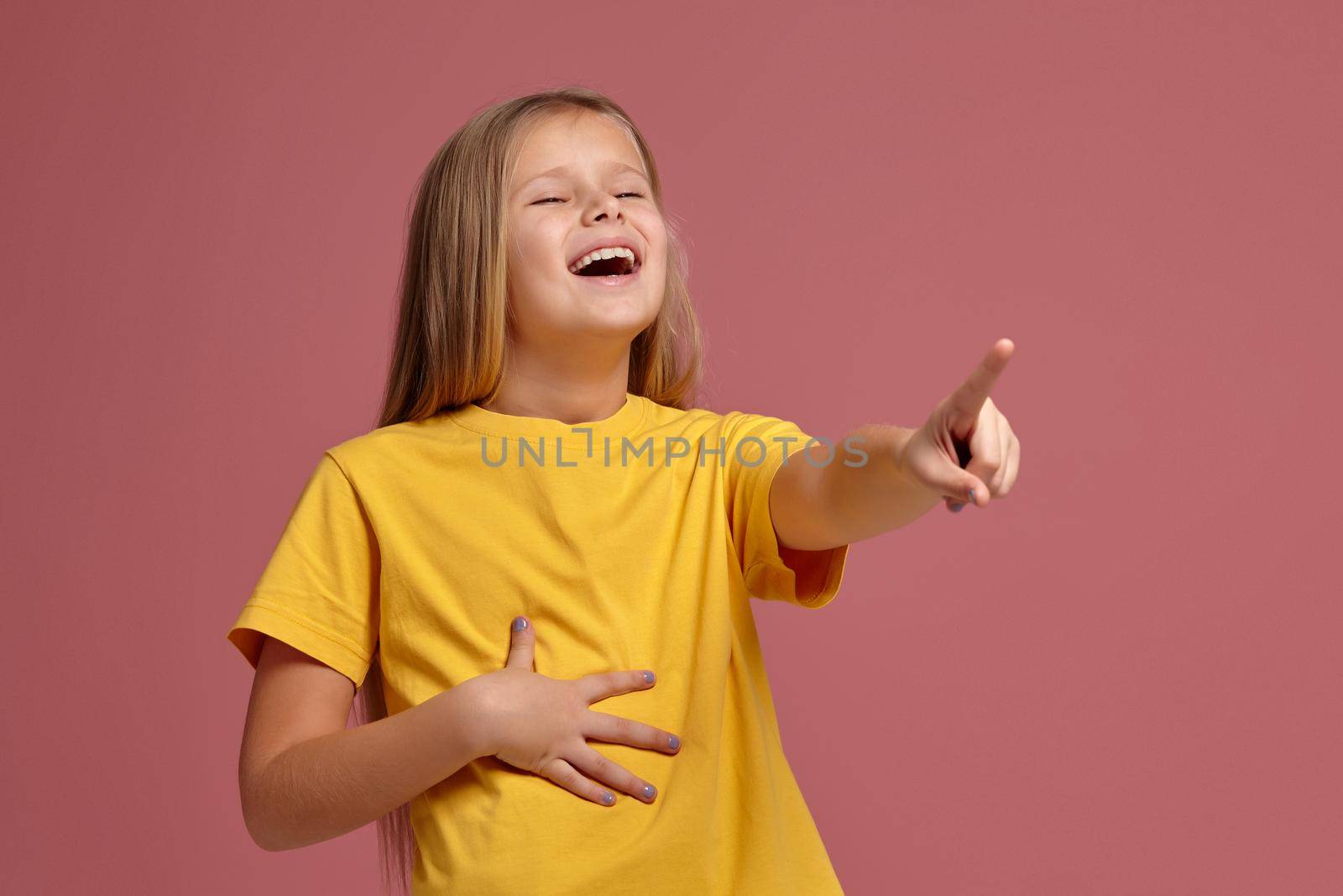 little girl in a yellow T-shirt on a coral background. laughs pointing finger
