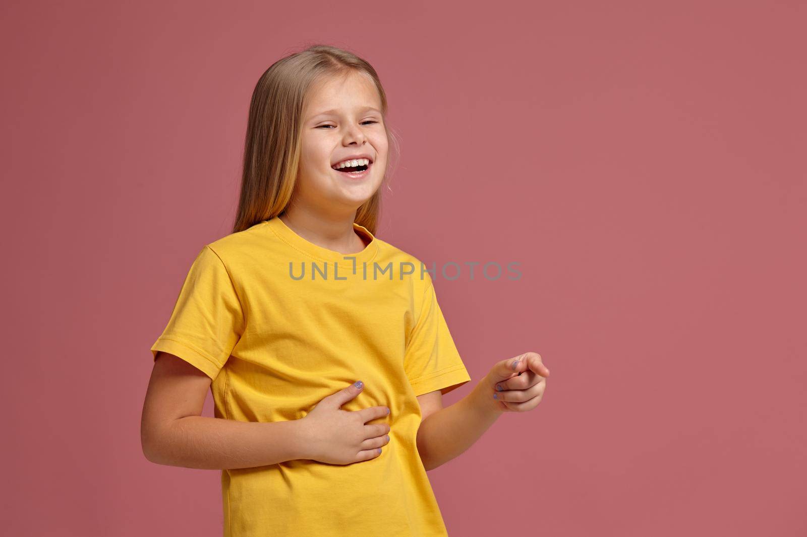 little girl in a yellow T-shirt on a coral background. laughs pointing finger