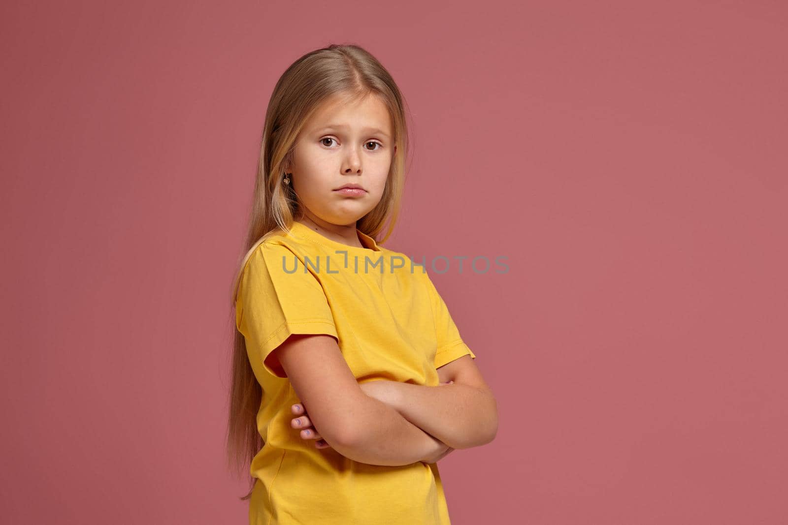 little girl in a yellow T-shirt on a coral background. looks offended