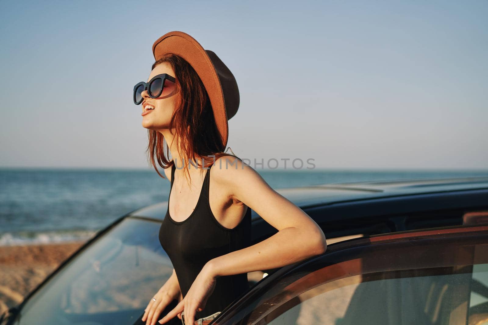 cheerful woman in sunglasses and a hat on the ocean near the car. High quality photo