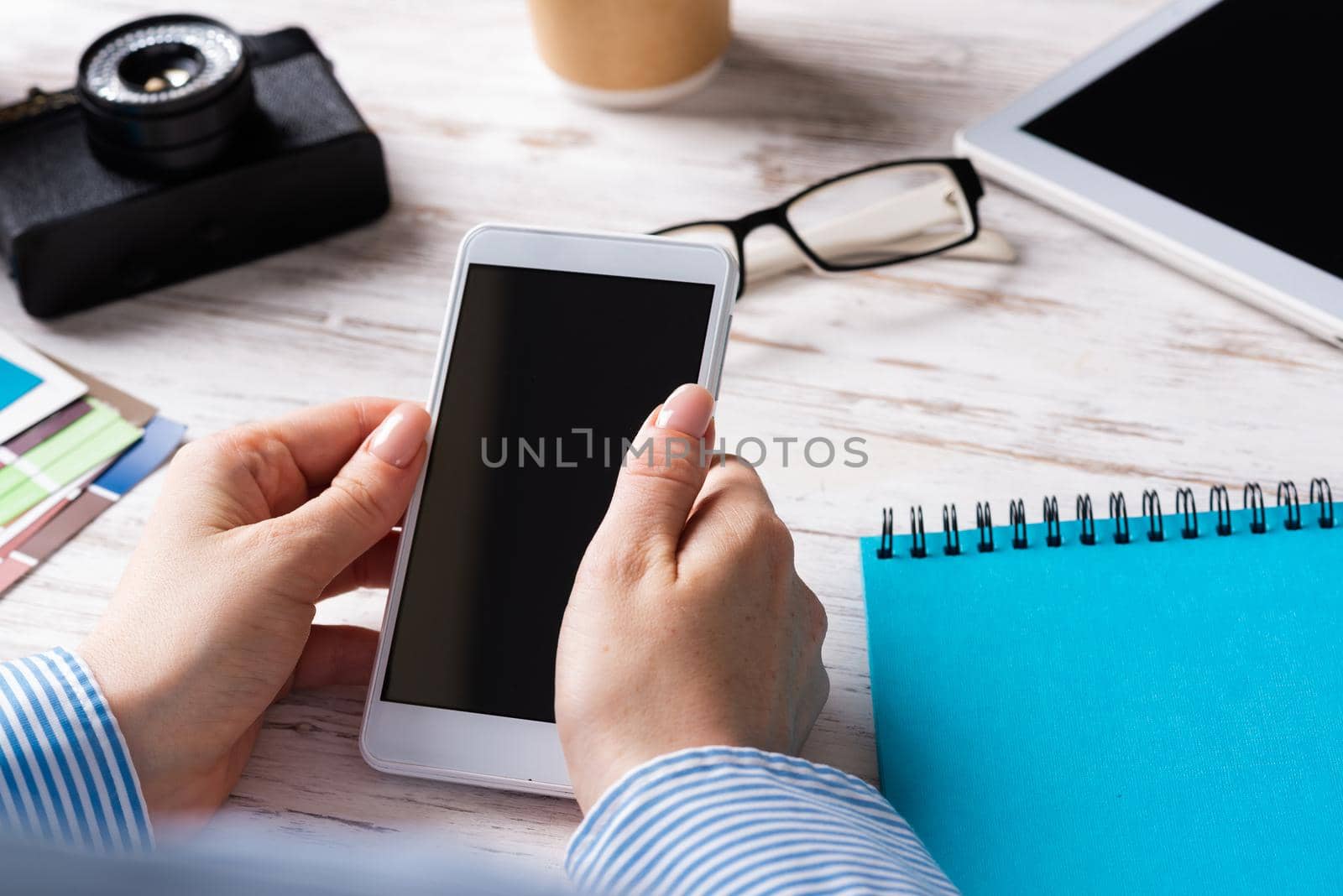Blogger sitting at desk and holding smartphone. Mobile smart devices in business processes. Business occupation and innovation. Corporate office workplace with business woman at wooden desk.