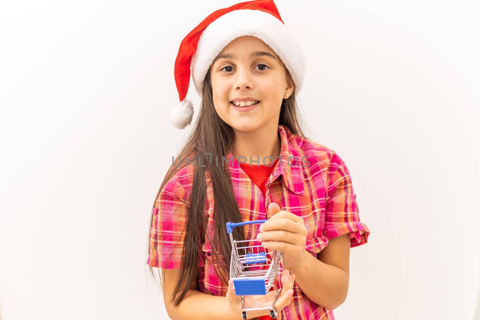 Full body little girl smiling and happy, holding a miniature shopping cart, concept of shopping, consumerism and christmas, can be used for internet purchases and commerce